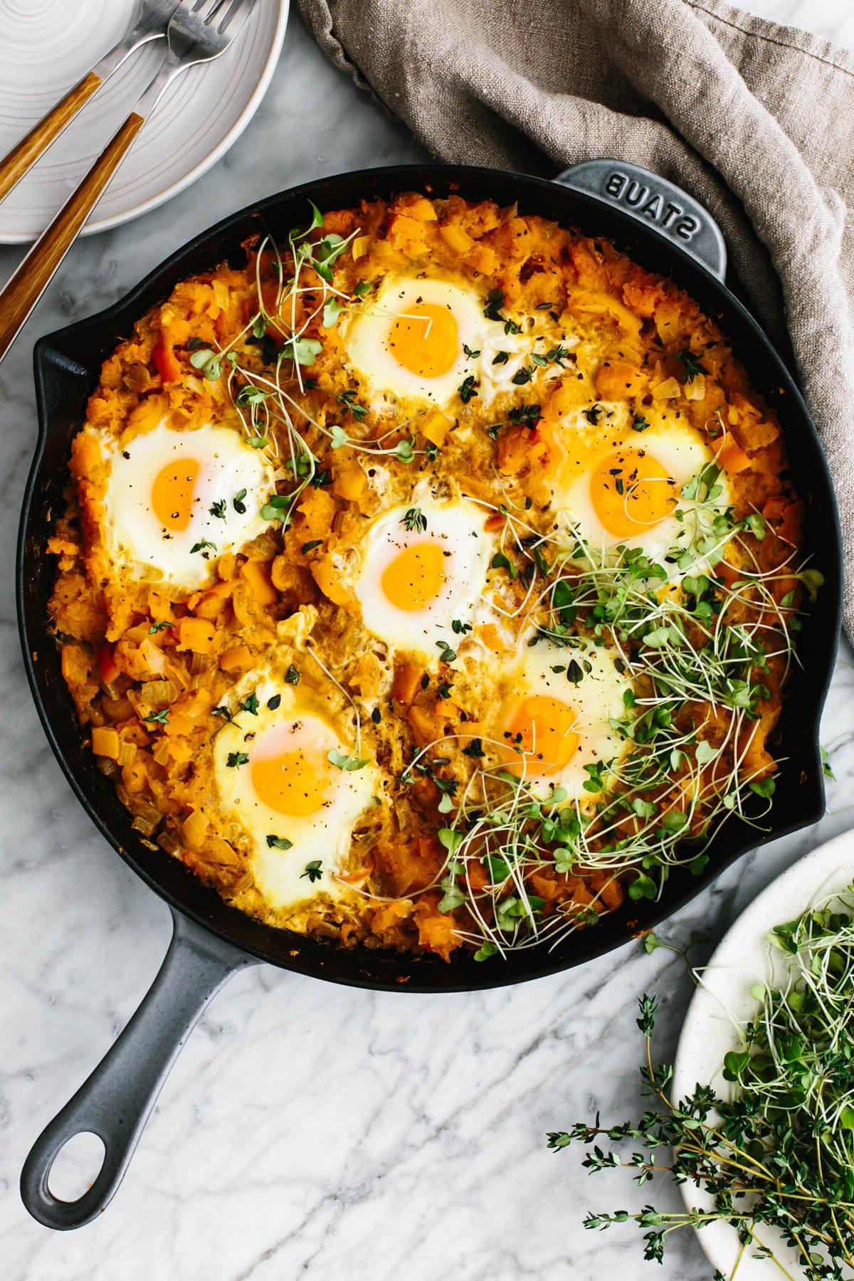 Die besten Butternusskürbis-Rezepte 2 Orangene Shakshuka in einer Pfanne auf einem Tisch.