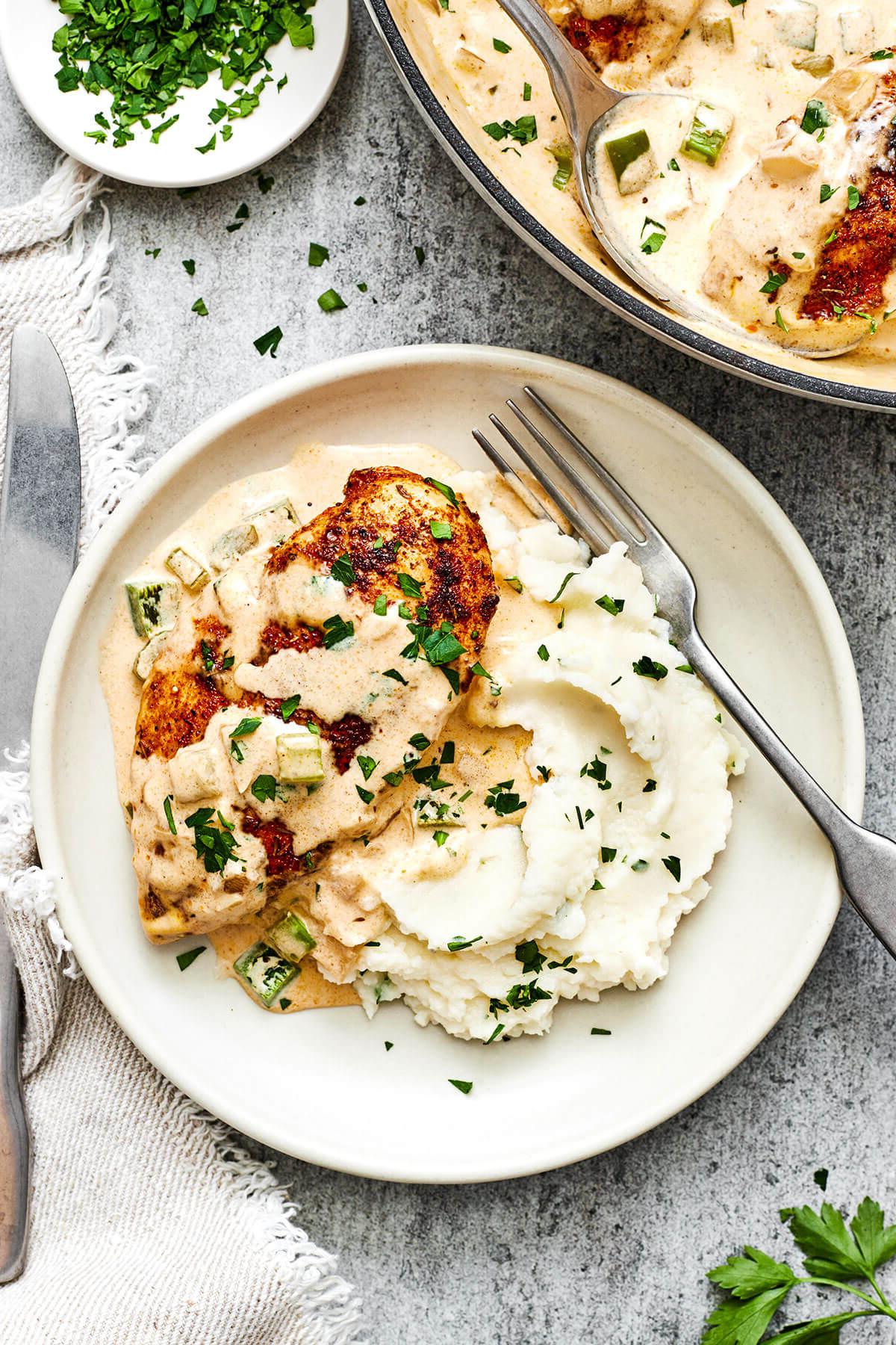 Mardi Gras Essensideen 2 Cajun Hähnchen mit cremigem Kartoffelpüree, verziert mit frischen Kräutern, auf einem gedeckten Tisch.