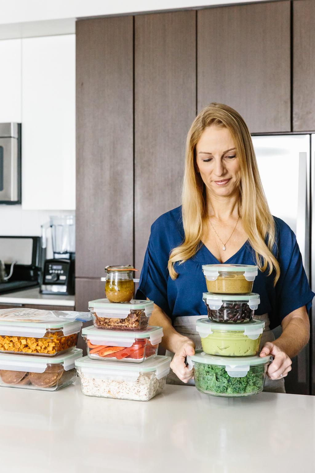 Eine Frau steht mit vorbereiteten Meal-Prep-Behältern voller saisonaler Zutaten und fertiger Mahlzeiten. Dieses Bild zeigt die Effizienz und Vielfalt des Herbst-Meal-Preps.