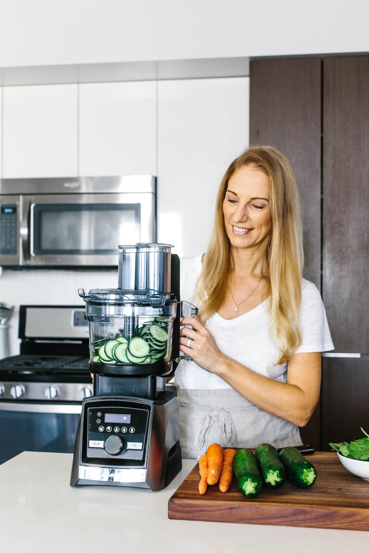 Mädchen betrachtet Vitamix Küchenmaschine mit geschnittenen Gurken darin.