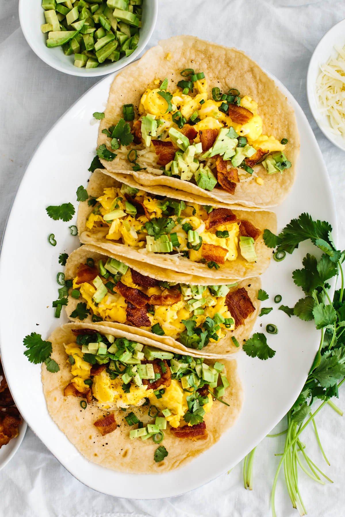 30+ Avocado Rezepte zum Genießen 11 Frühstücks-Tacos auf einem Teller neben Koriander und Avocado.