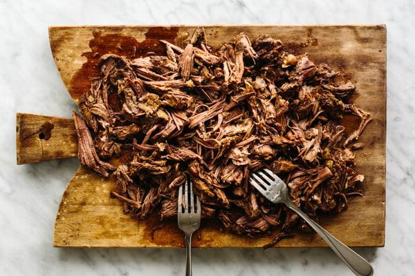 Rinder-Barbacoa auf einem Schneidebrett zerzupfen.