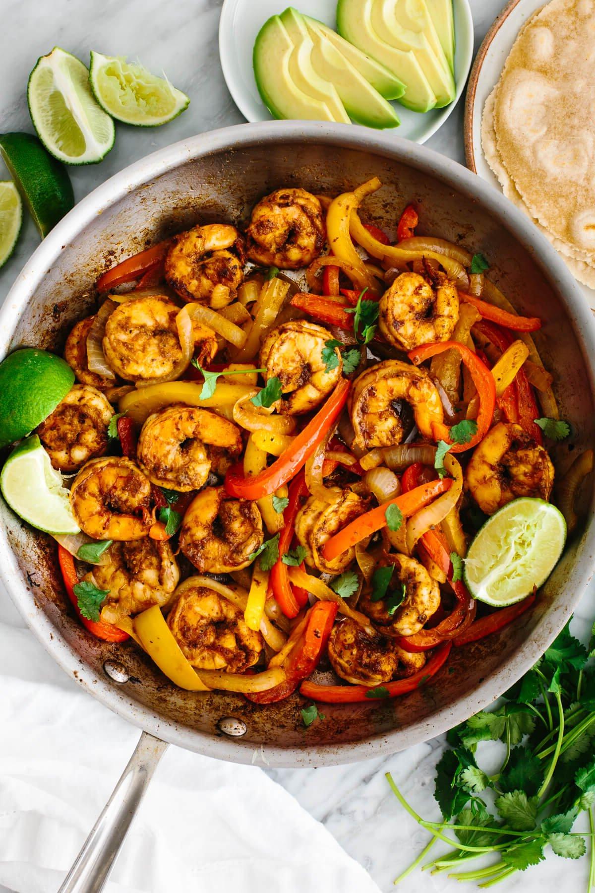 10+ beste Garnelenrezepte 12 Garnelen-Fajitas in einer Pfanne mit Avocadoscheiben und Limettenspalten.