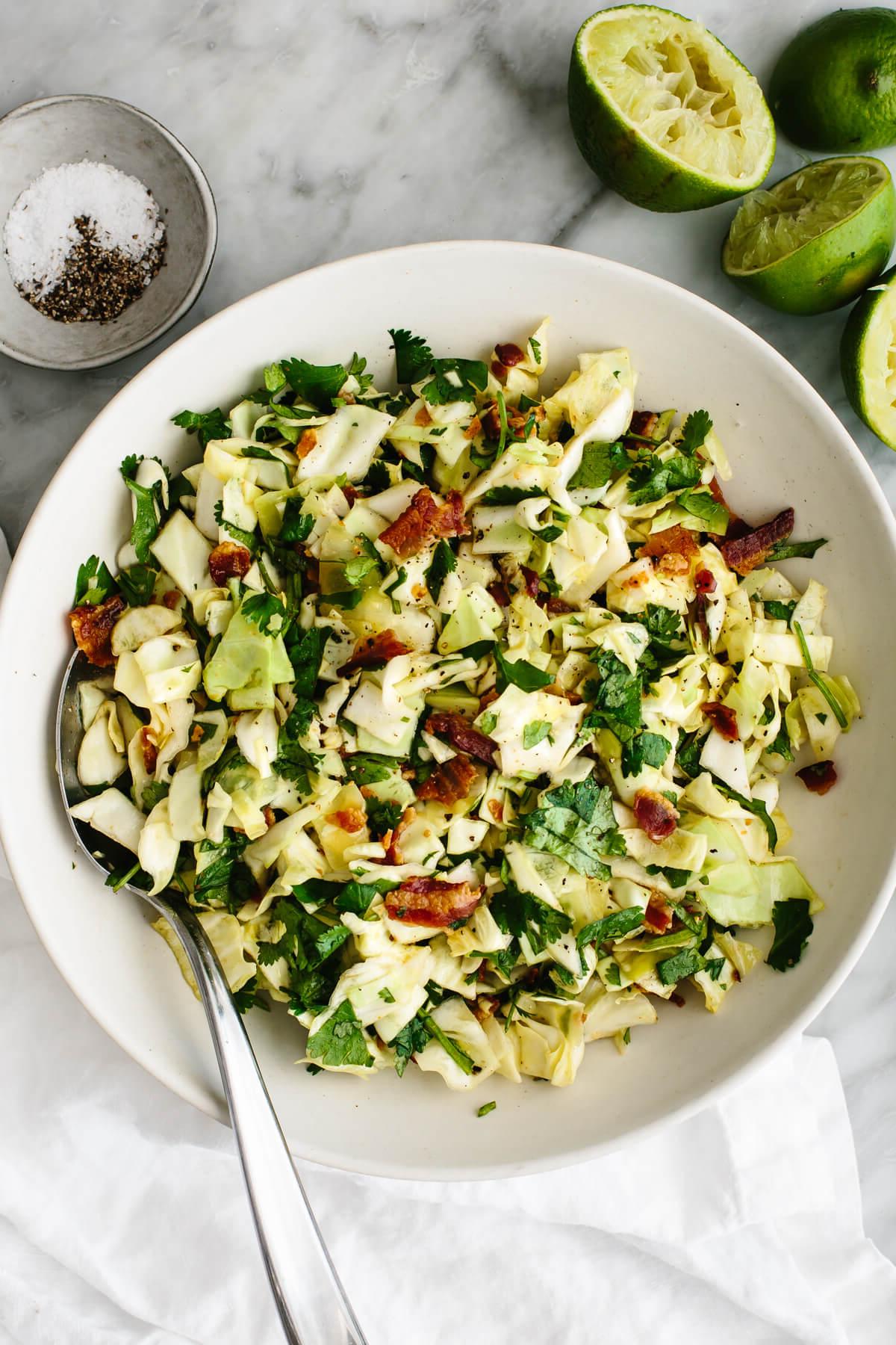 10+ leckere Kohlrezepte zum Verlieben 12 Koriander-Limette-Speck-Krautsalat in einer großen weißen Schüssel mit einem Löffel.