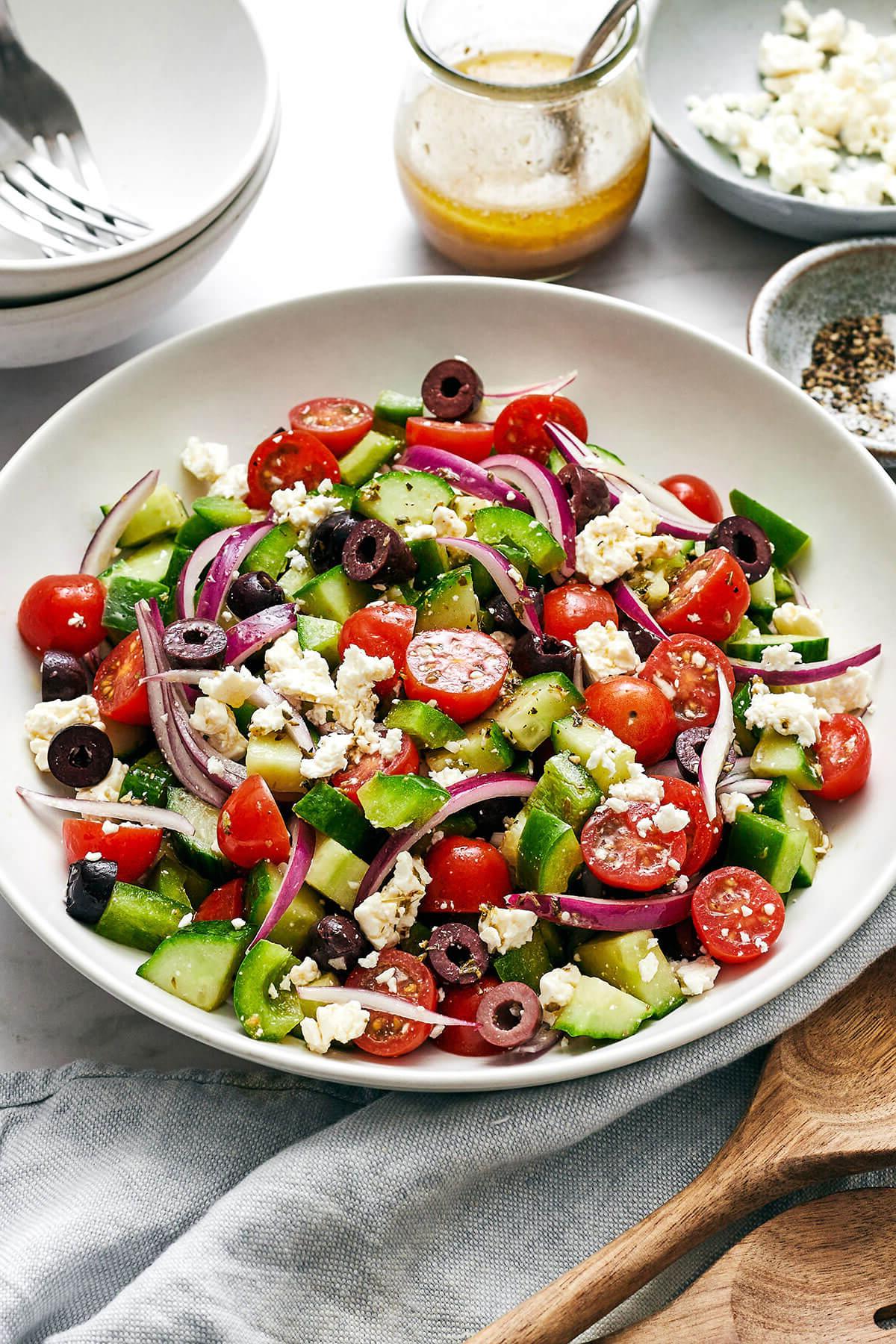 Die 60+ besten Mittelmeer-Diät-Rezepte 12 Griechischer Salat in einer weißen Schüssel neben Dressing.