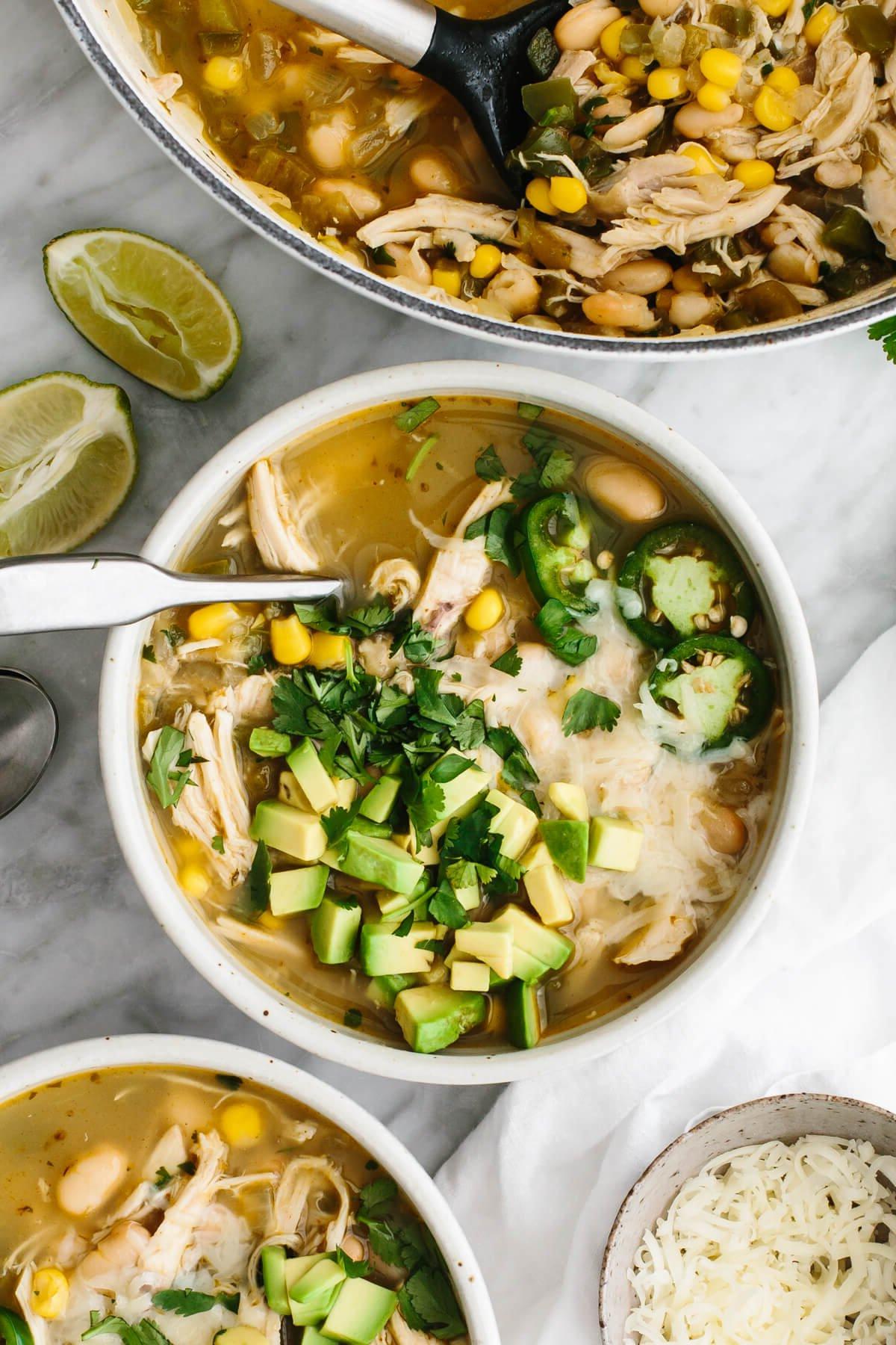 30+ Avocado Rezepte zum Genießen 13 Weißer Hähnchen-Chili in einer Schüssel neben einem Topf davon.