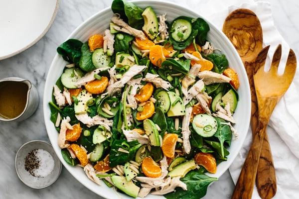 Eine Schüssel Mandarin-Hähnchensalat neben Servierlöffeln.