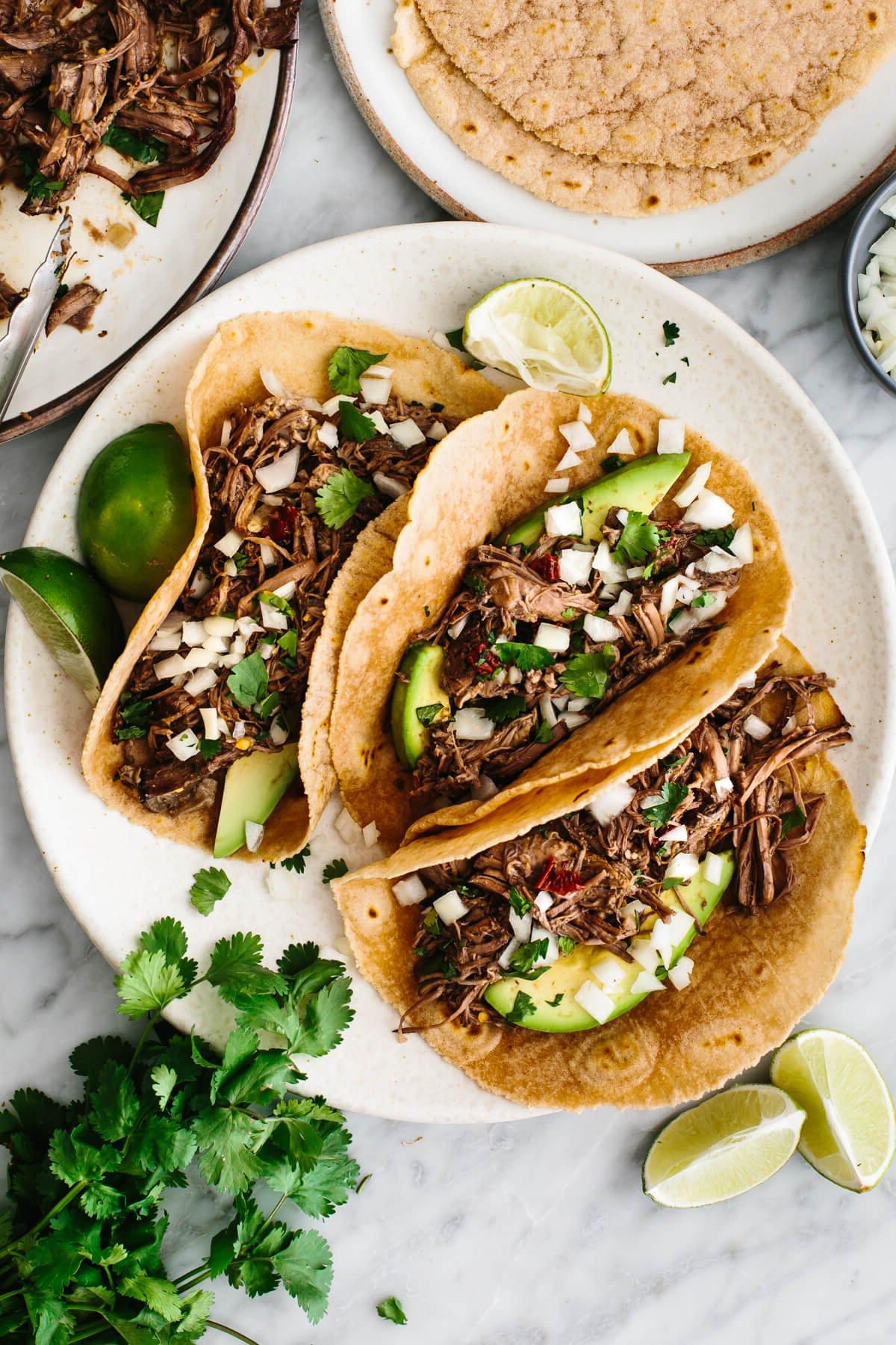 30+ Avocado Rezepte zum Genießen 14 Barbacoa-Tacos auf einem Teller mit Koriander und Limettenspalten.