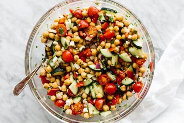Zutaten für den mediterranen Kichererbsensalat in einer Glasschüssel auf einem Tisch vermischt.