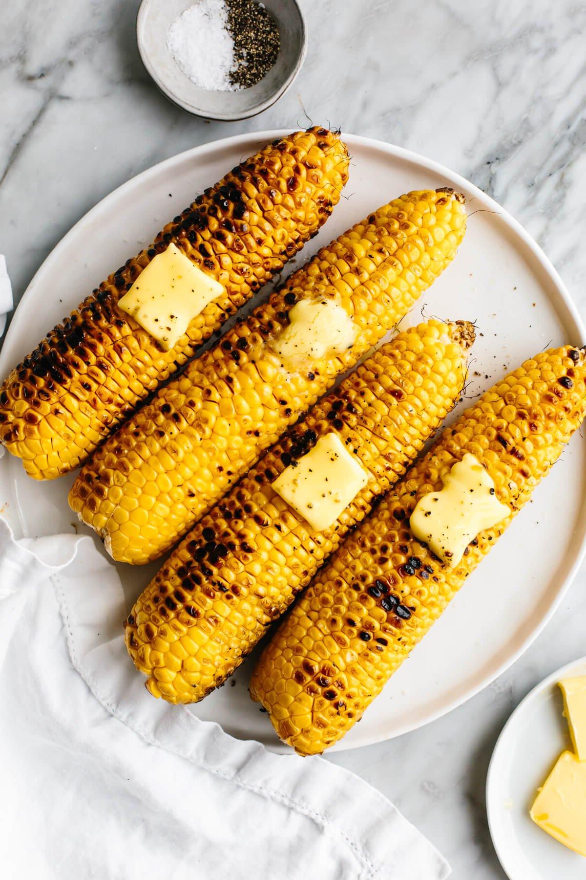 Über 30 festliche Rezepte zum 4. Juli 16 Gegrillte Maiskolben auf einem weißen Teller neben Butter.