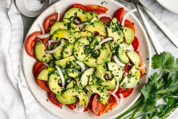 Ein Teller Tomaten-, Zwiebel-, Avocado-Salat neben Gabeln