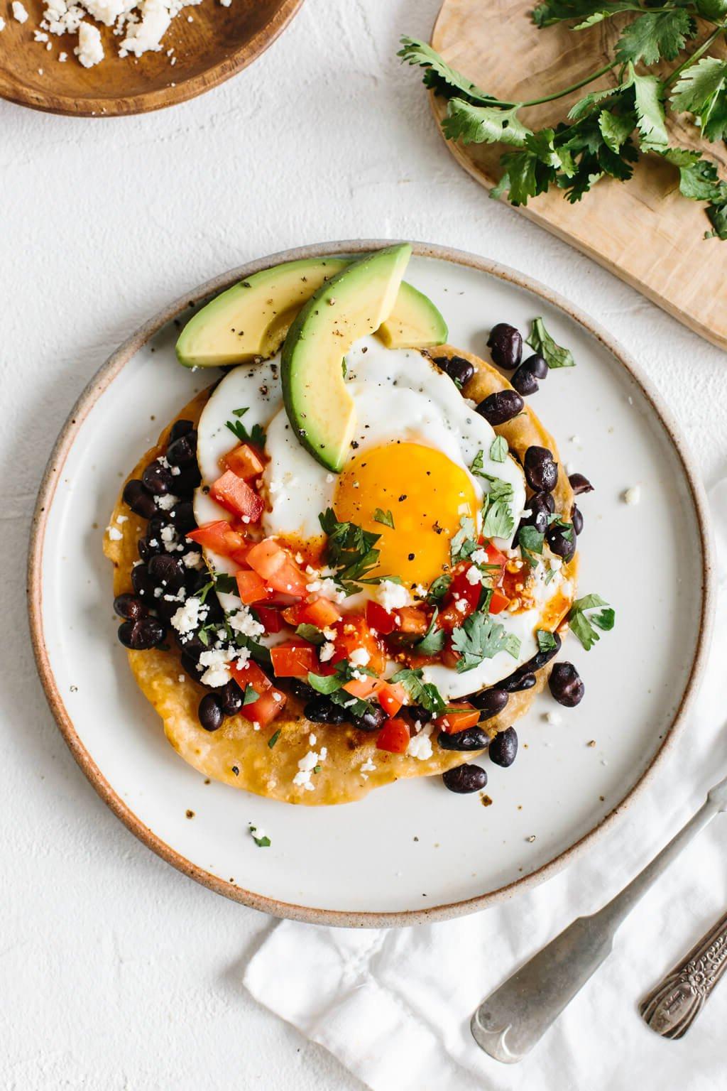 Über 40 Beste Gesunde Frühstücksideen 3 Huevos Rancheros auf einem weißen Teller, belegt mit Avocadoscheiben.