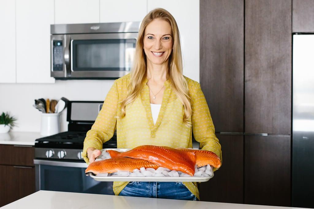 Mädchen in der Küche, das Sockeye-Lachs und Königslachs auf einer Platte hält.