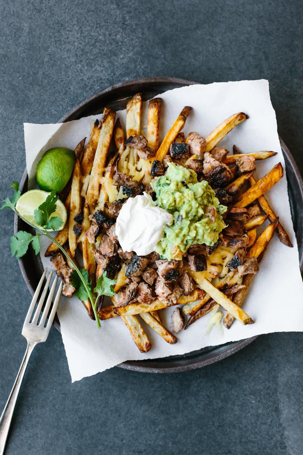 30+ Mexikanische Rezepte – Perfekt für den Cinco de Mayo 28 Pommes Frites belegt mit Carne Asada, Guacamole und Sauerrahm auf einem Teller.