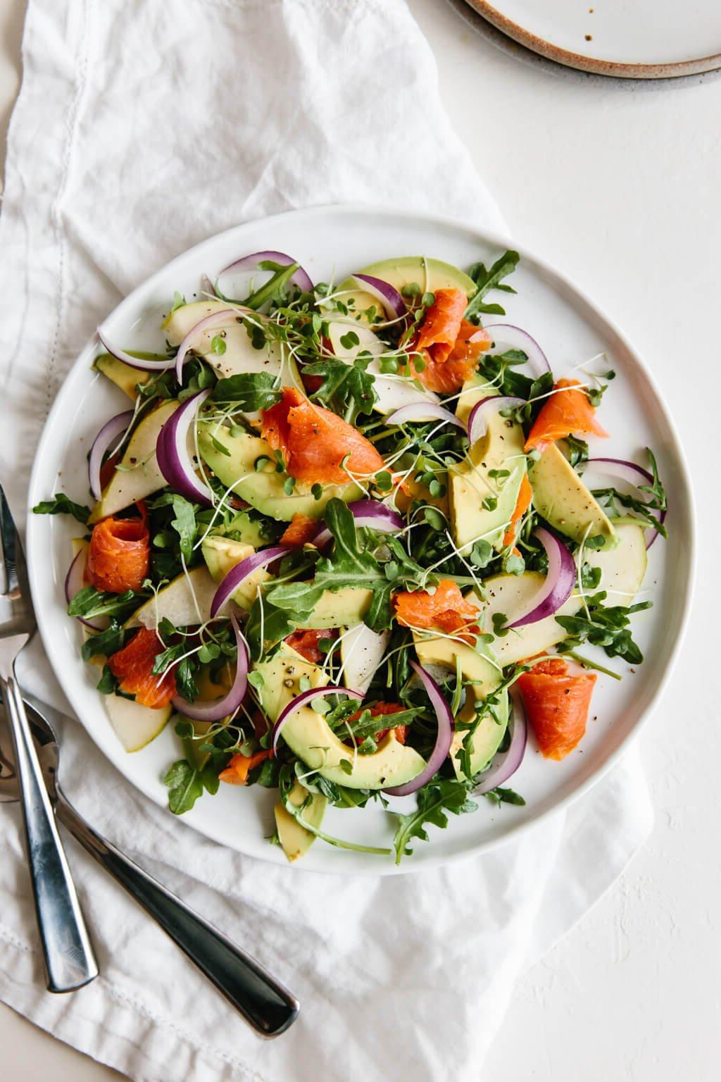 Ein einfaches und köstliches Rucola-Salat-Rezept mit Baby-Rucola, geräuchertem Lachs, Avocado, Birne und roter Zwiebel.