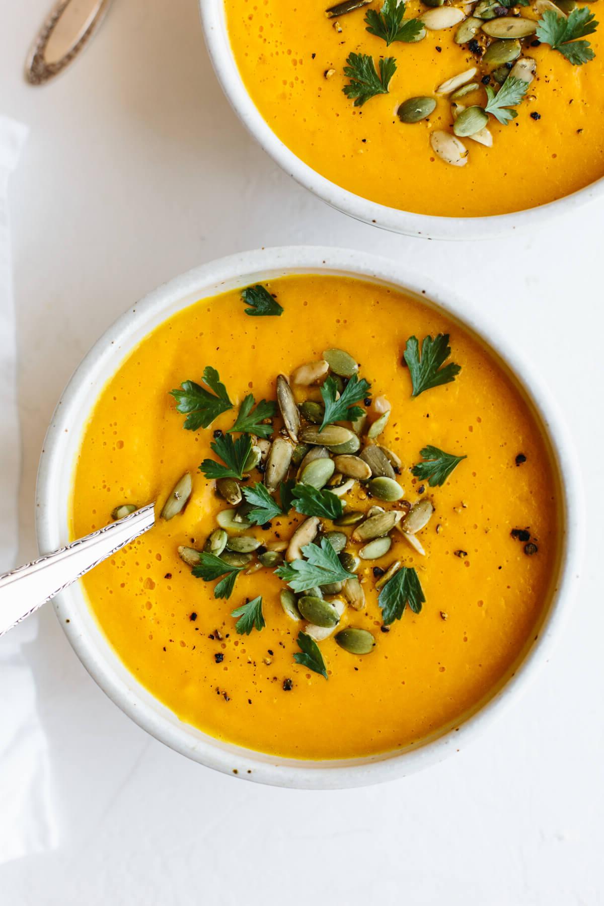 Die besten Butternusskürbis-Rezepte 4 Zwei Schüsseln Butternusskürbiscremesuppe mit Löffeln.