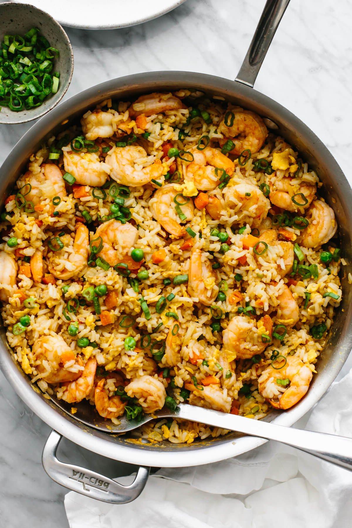 10+ beste Garnelenrezepte 4 Eine Pfanne mit Garnelen-Gebratenem Reis mit einem Servierlöffel.