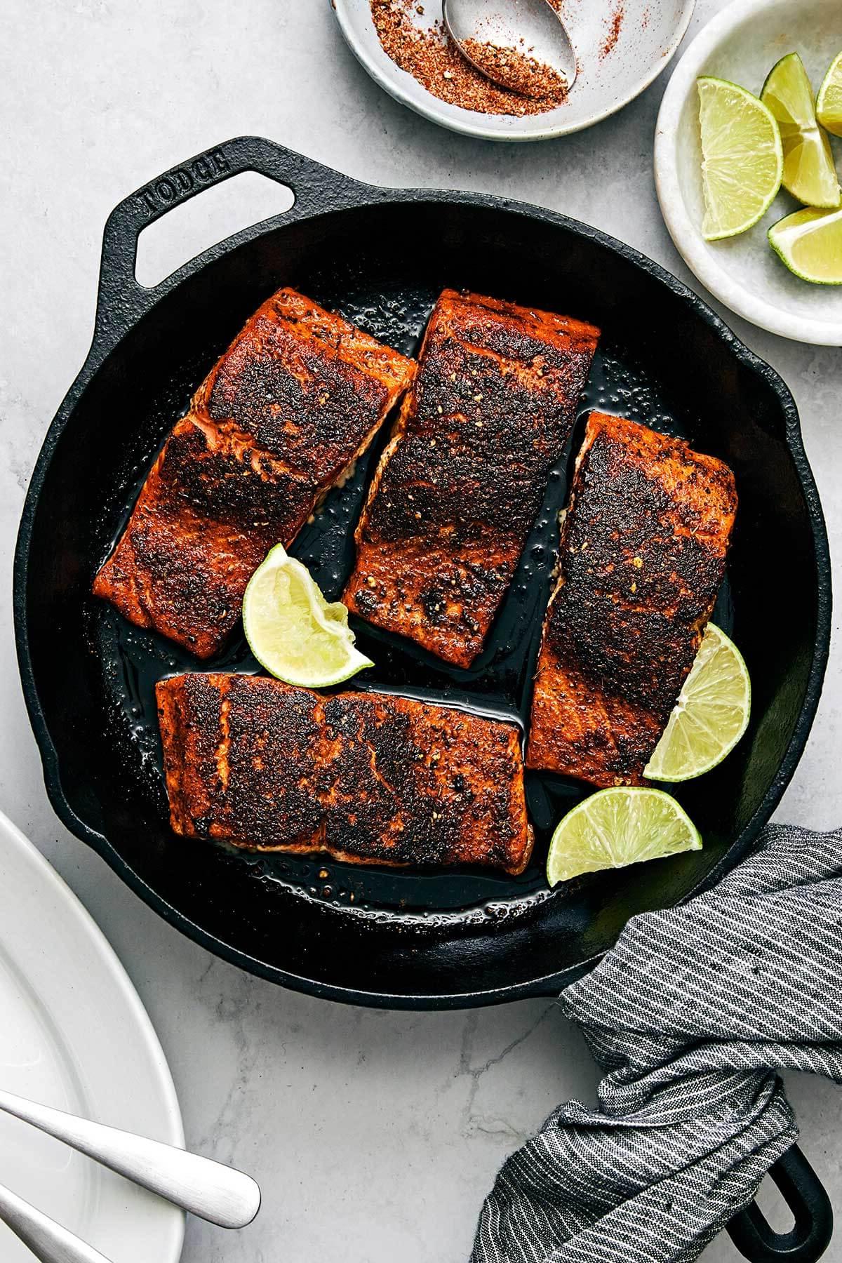 Mardi Gras Essensideen 4 Ein Stück Blackened Salmon mit knuspriger Kruste in einer heißen gusseisernen Pfanne, garniert mit frischen Kräutern.