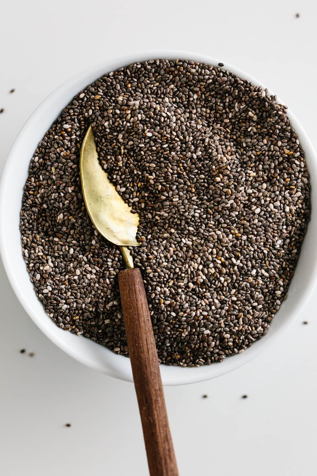 Chiasamen sind kleine, aber mächtige Samen mit zahlreichen gesundheitlichen Vorteilen! Chiasamen in einer weißen Schale mit einem goldenen Löffel.