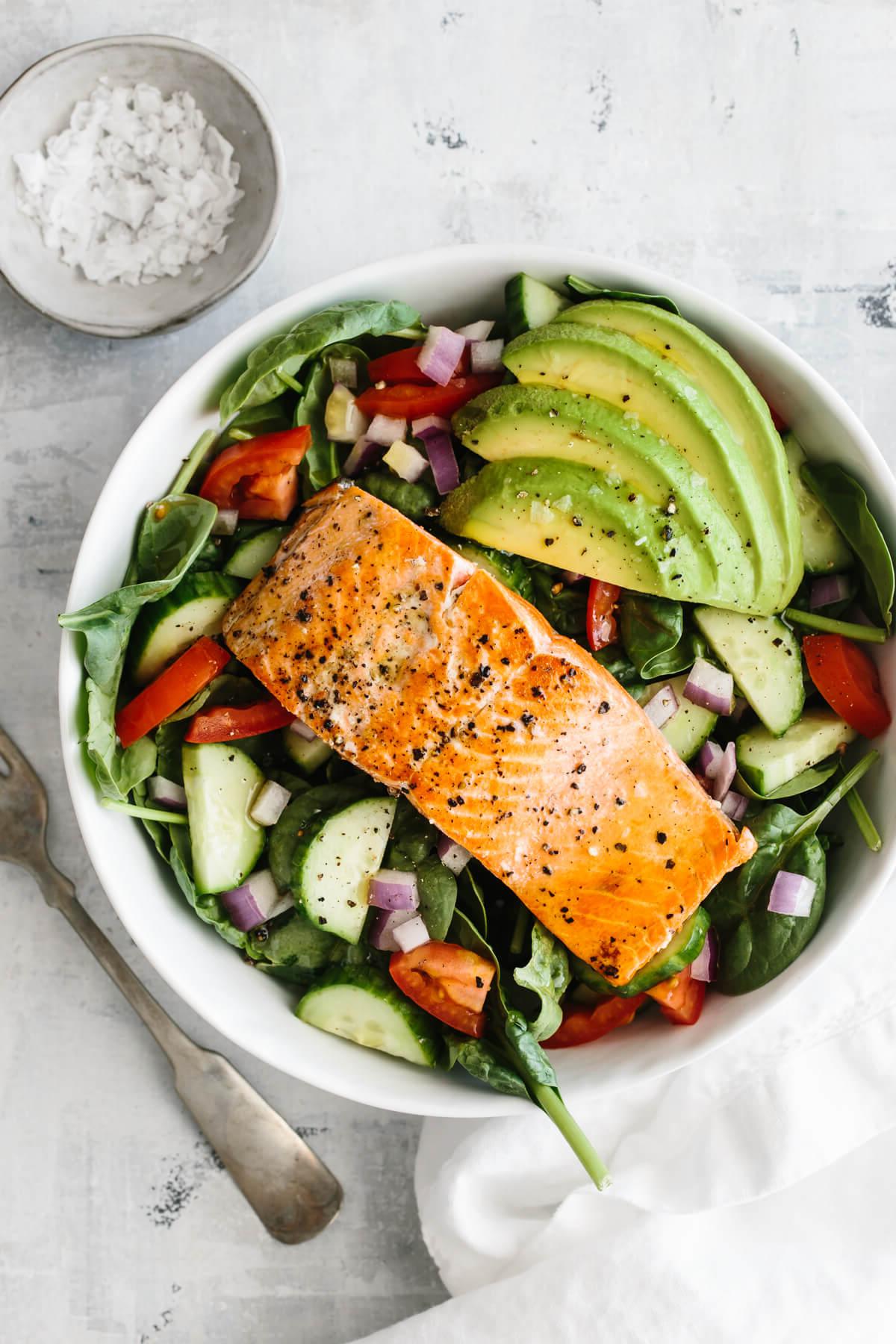 Über 50 einfache Whole30 Abendessen-Rezepte 4 Einzelnes Lachsfilet auf Salat mit Avocado und einer Schüssel mit einer Prise Salz daneben.