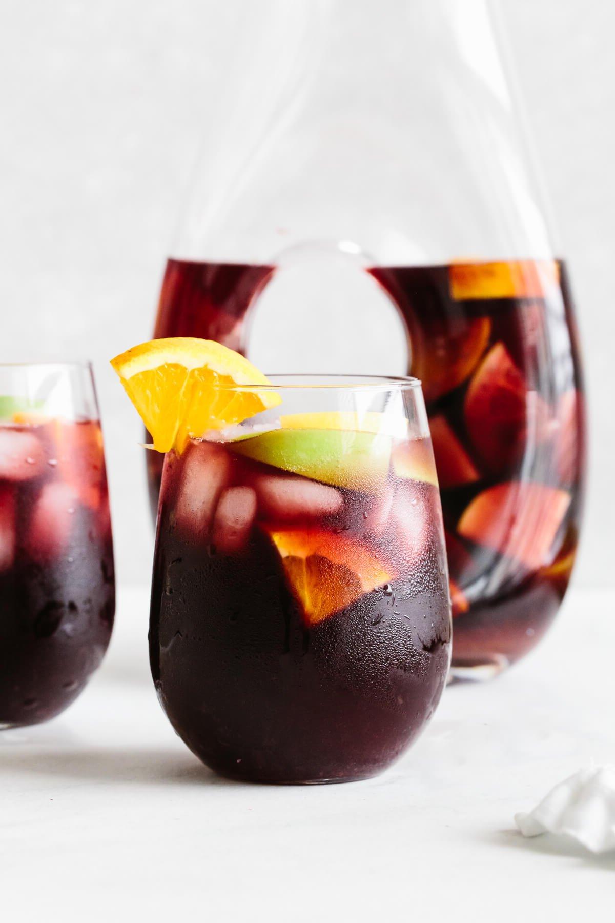 Über 30 festliche Rezepte zum 4. Juli 33 Rote Sangria in einem Glas mit Orangenscheibe als Garnierung und Krug im Hintergrund.