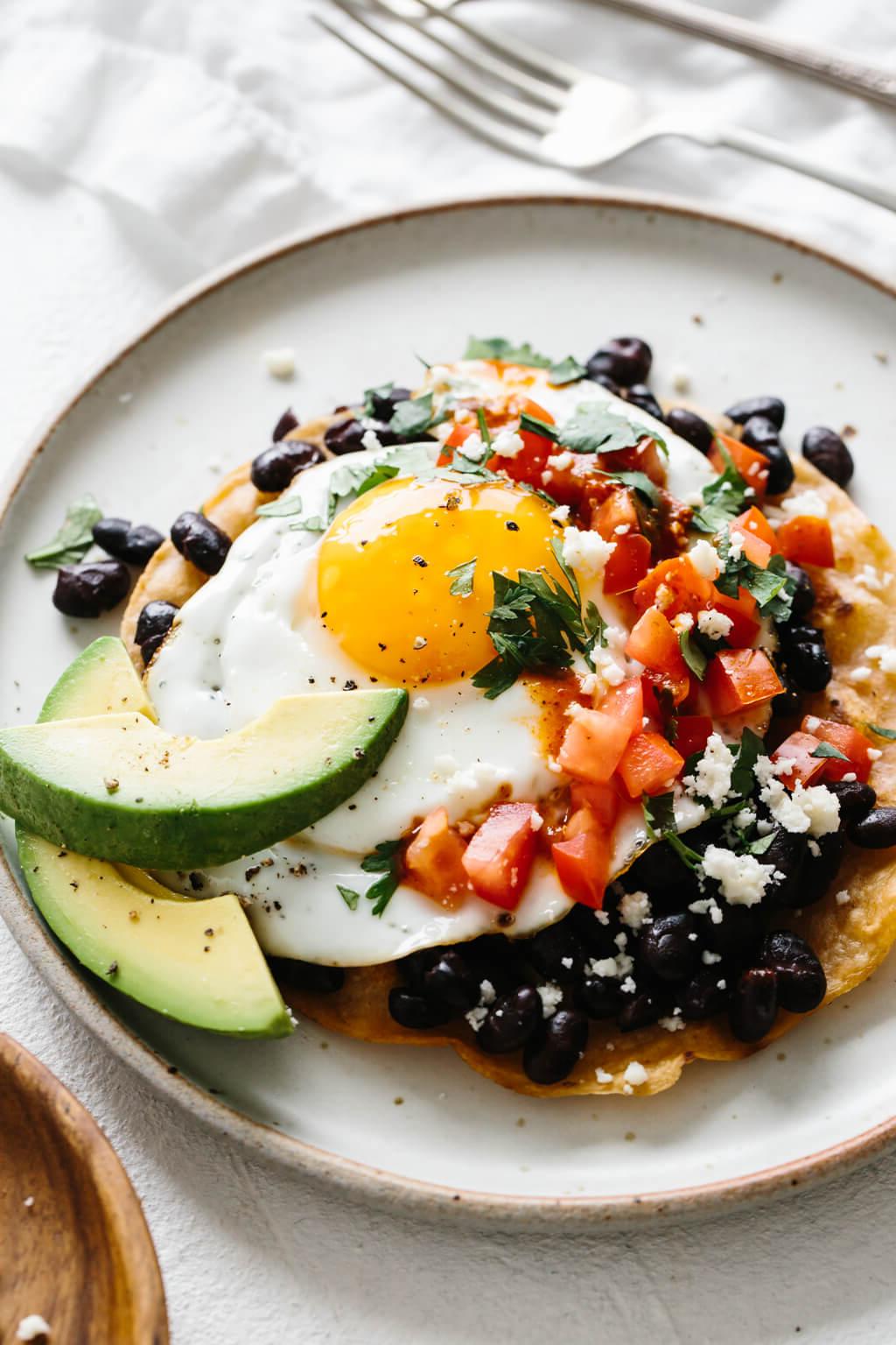 30+ Mexikanische Rezepte – Perfekt für den Cinco de Mayo 34 Huevos Rancheros auf einem weißen Teller neben Gabeln.