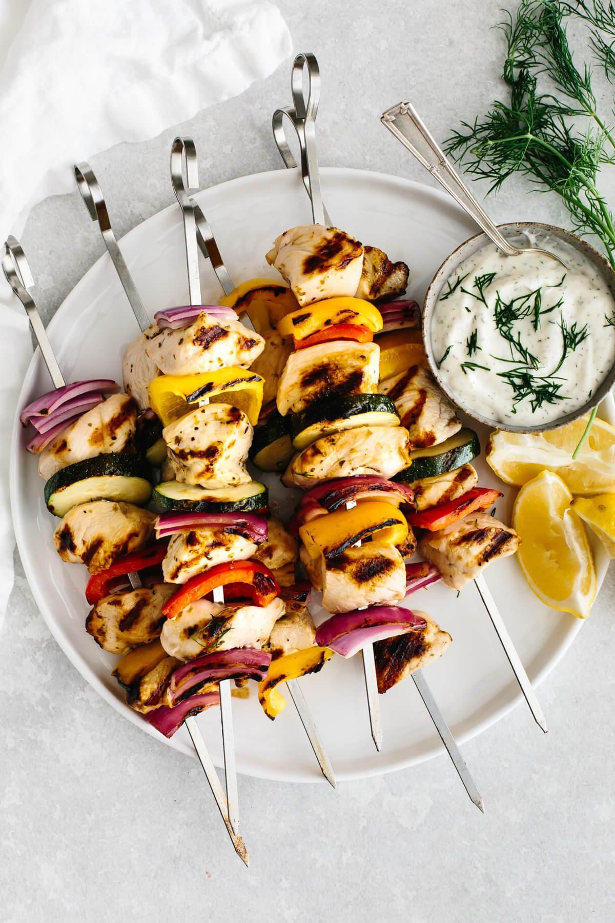 Über 50 einfache Whole30 Abendessen-Rezepte 37 Ein Teller voller gekochter Hähnchenspieße, daneben Tzatziki-Sauce.