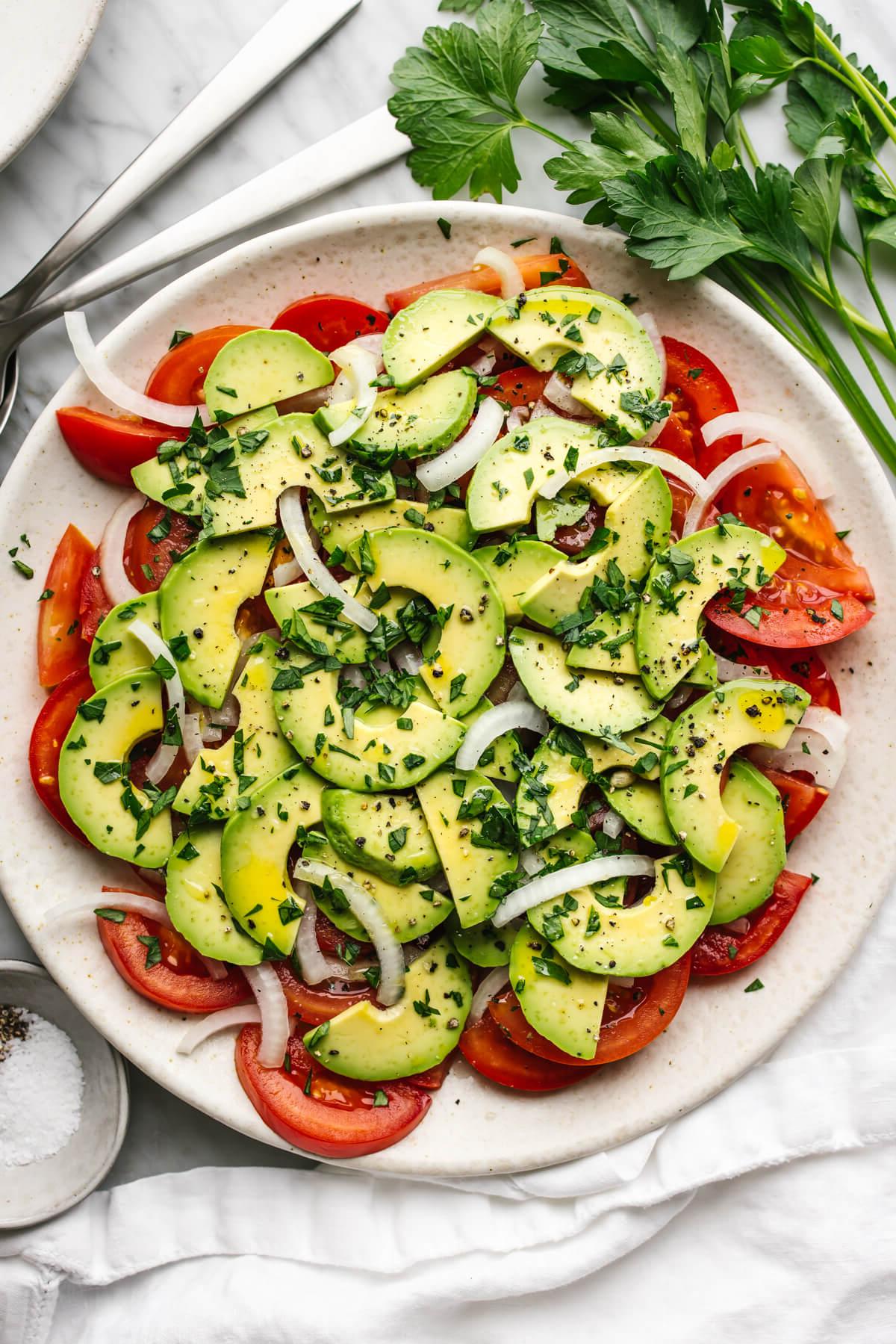 Die 60+ besten Mittelmeer-Diät-Rezepte 39 Tomaten-, Zwiebel-, Avocado-Salat auf einem Teller neben Petersilie.