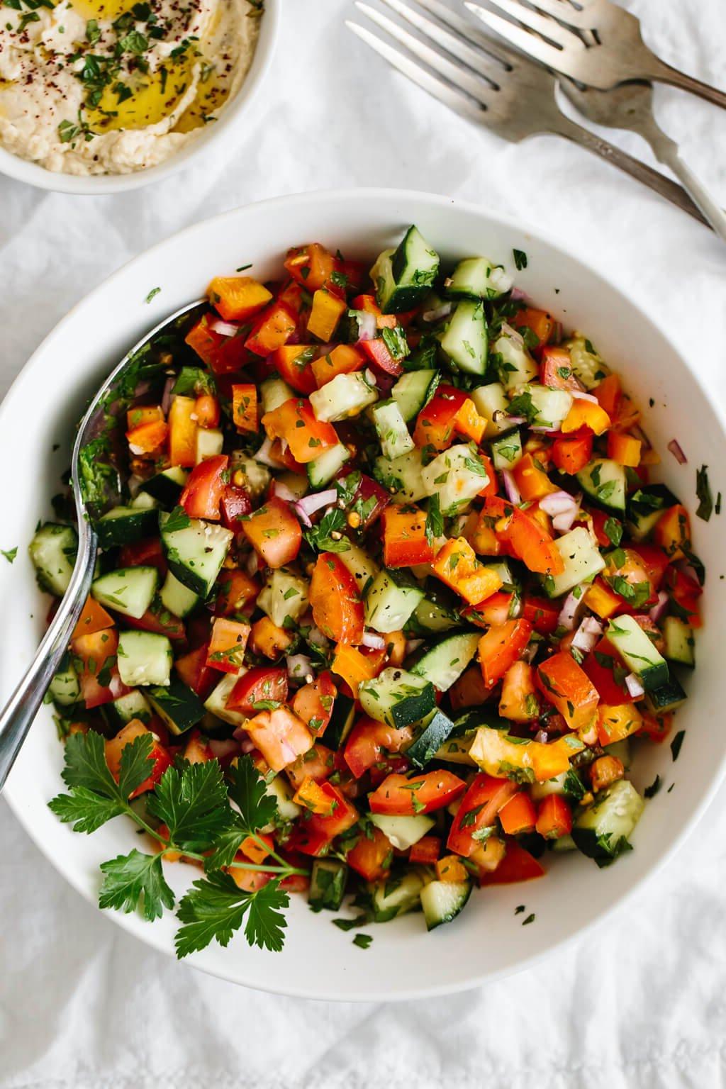 Die 60+ besten Mittelmeer-Diät-Rezepte 40 Israelischer Salat aus Tomaten, Gurken, Paprika, roten Zwiebeln und Kräutern in einer weißen Schüssel.