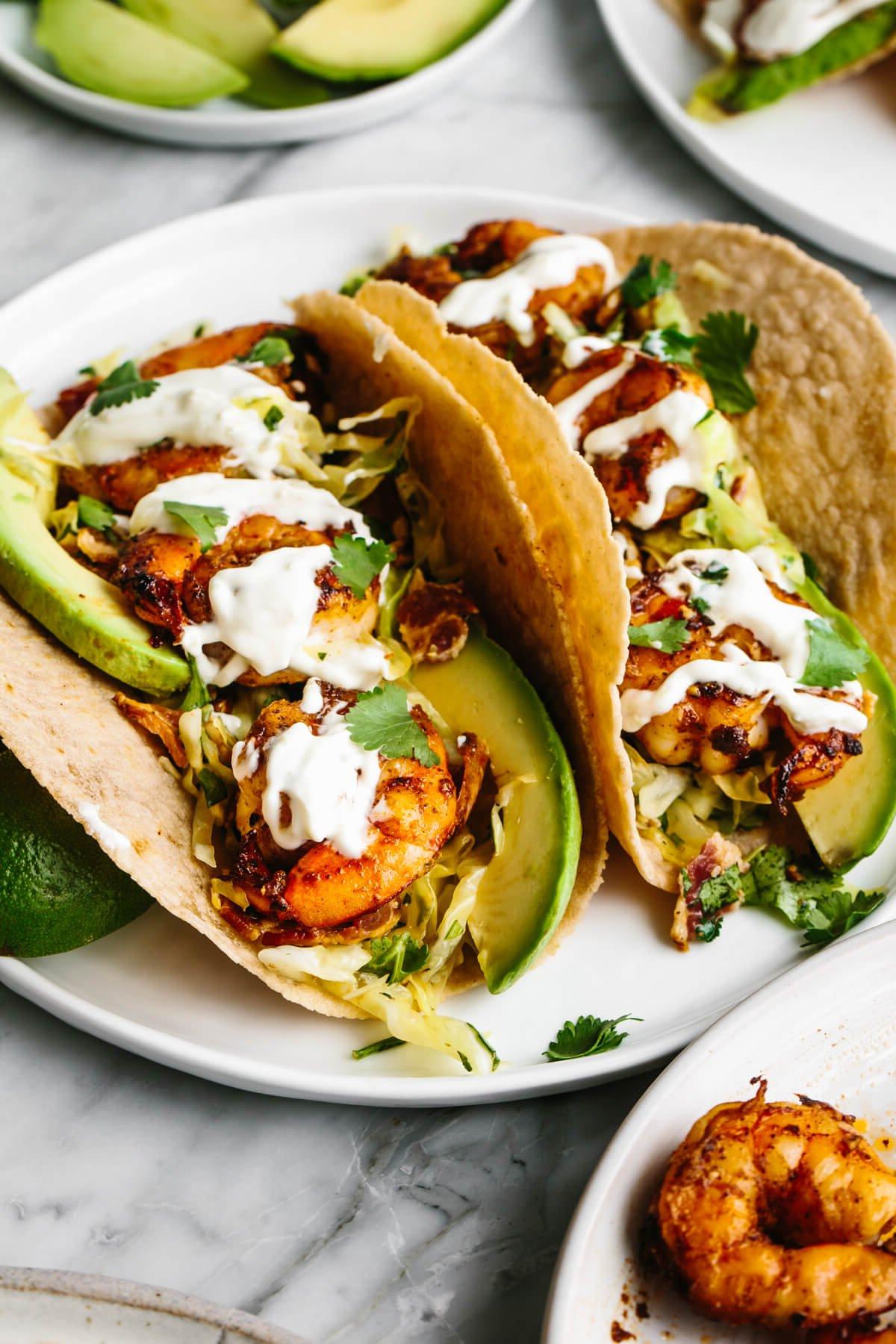 10+ beste Garnelenrezepte 5 Garnelen-Tacos auf einem Teller neben Avocado.