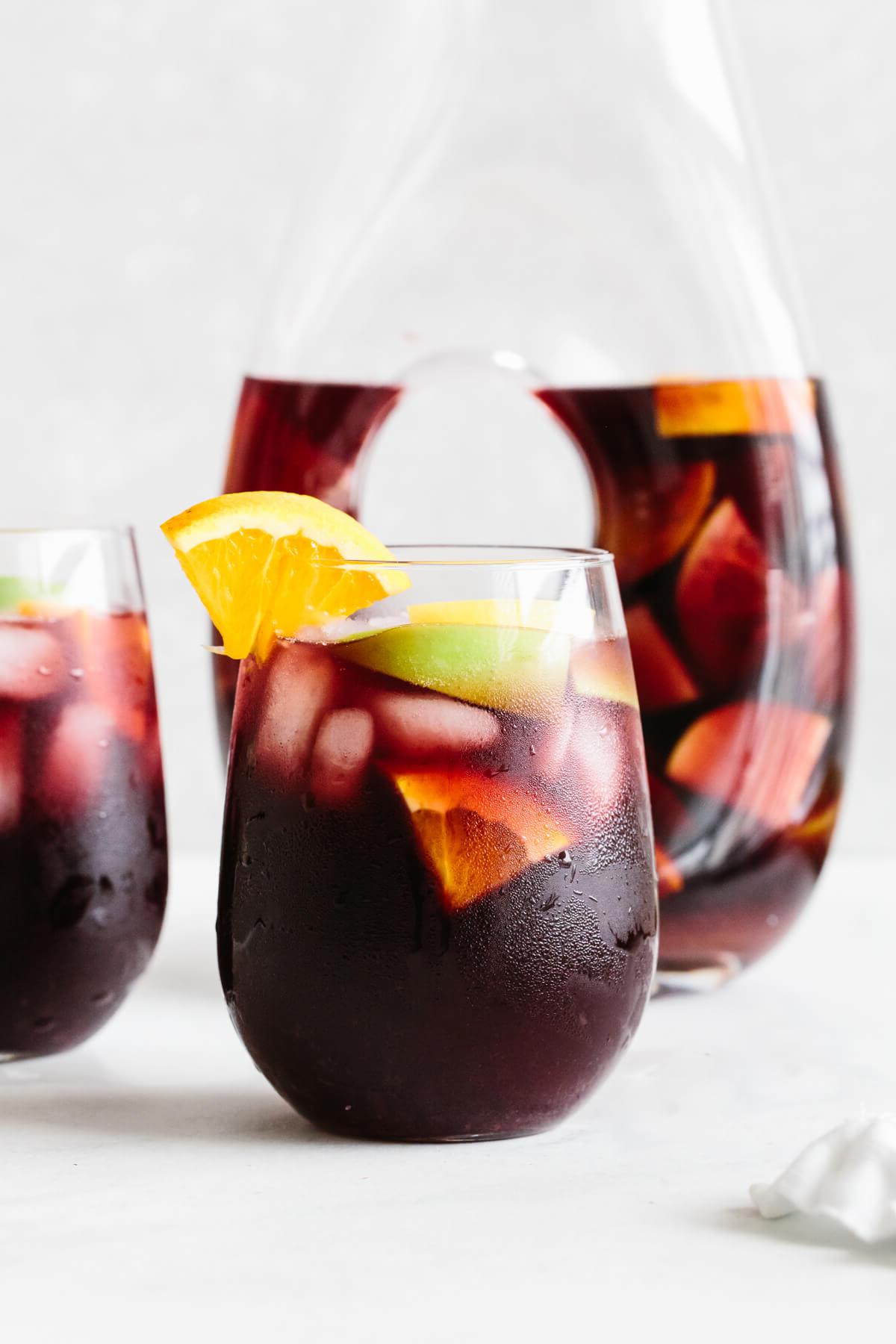 25+ Beste Memorial Day Rezepte 4 Rote Sangria in einem Glas mit Orangenscheibe als Garnitur, Krug im Hintergrund.