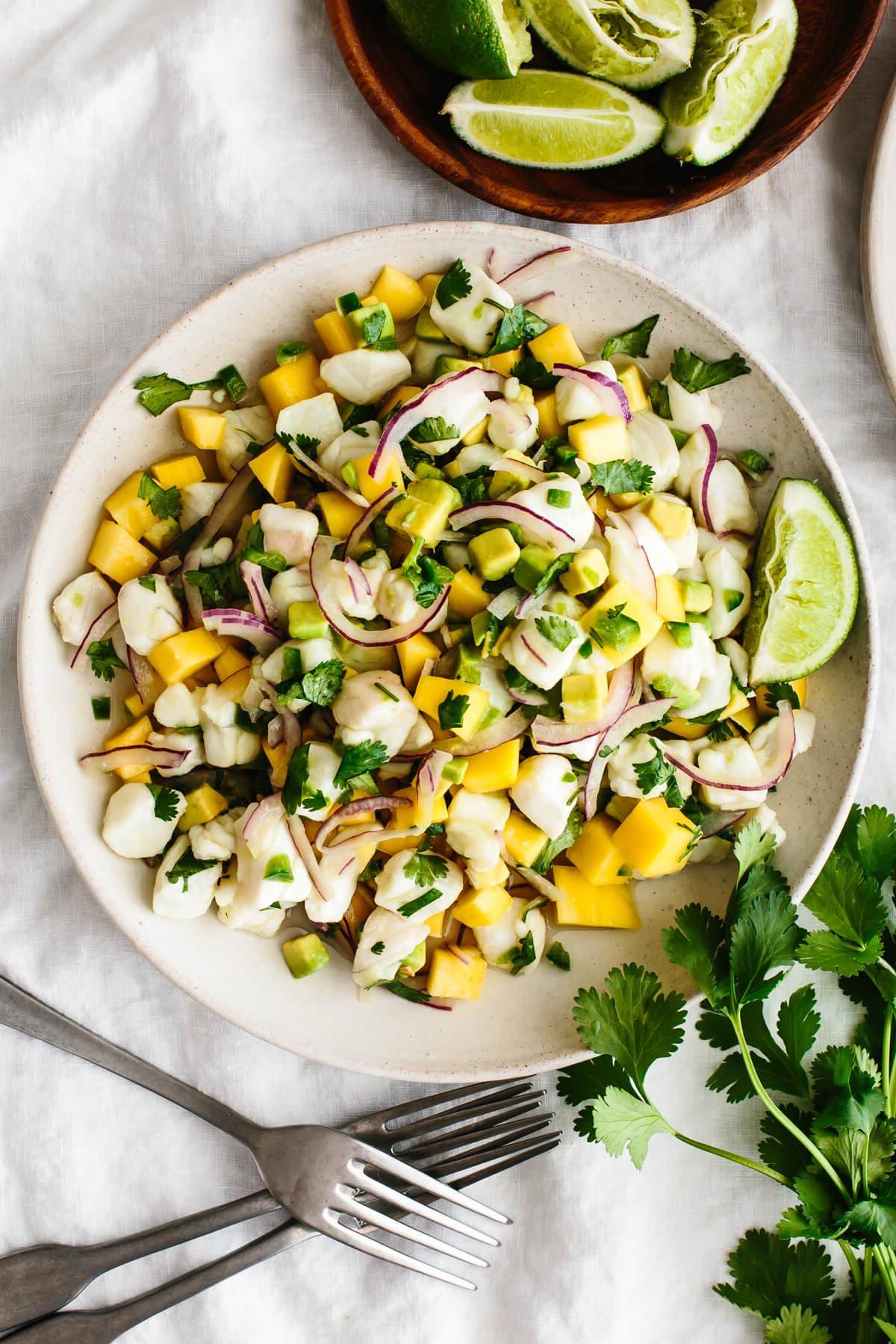 30+ Avocado Rezepte zum Genießen 6 Mango-Heilbutt-Ceviche auf einem Teller neben Koriander und Limetten.