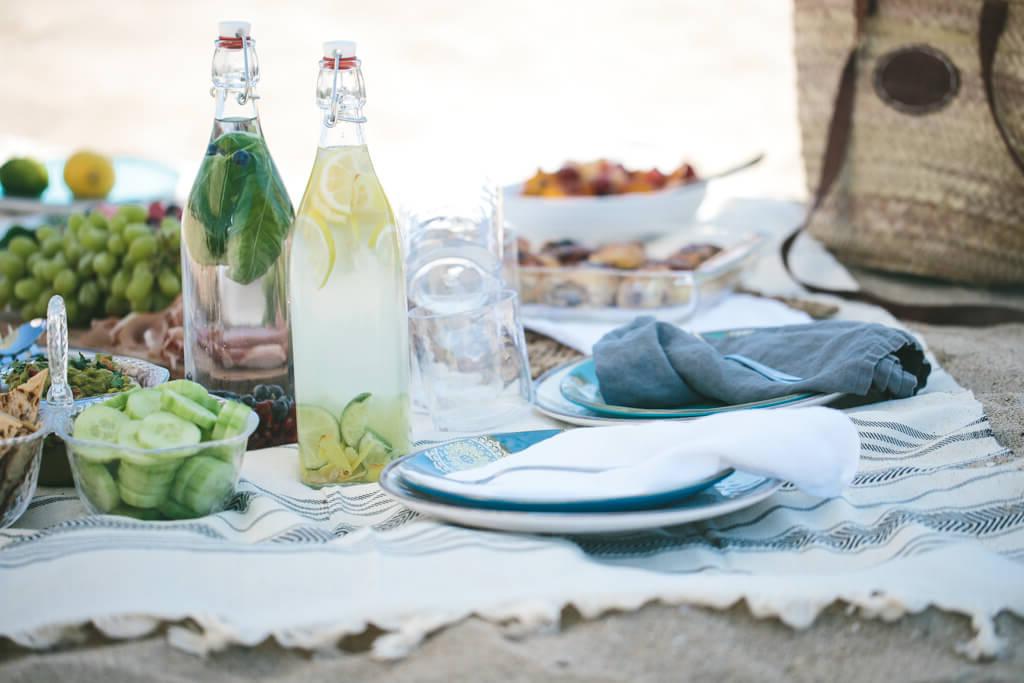 Gesunde Rezepte für den Tag der Arbeit, perfekt für ein Picknick, Grillfest oder eine Party! Strandpicknick auf einem Handtuch mit Flaschen Infusionswasser.