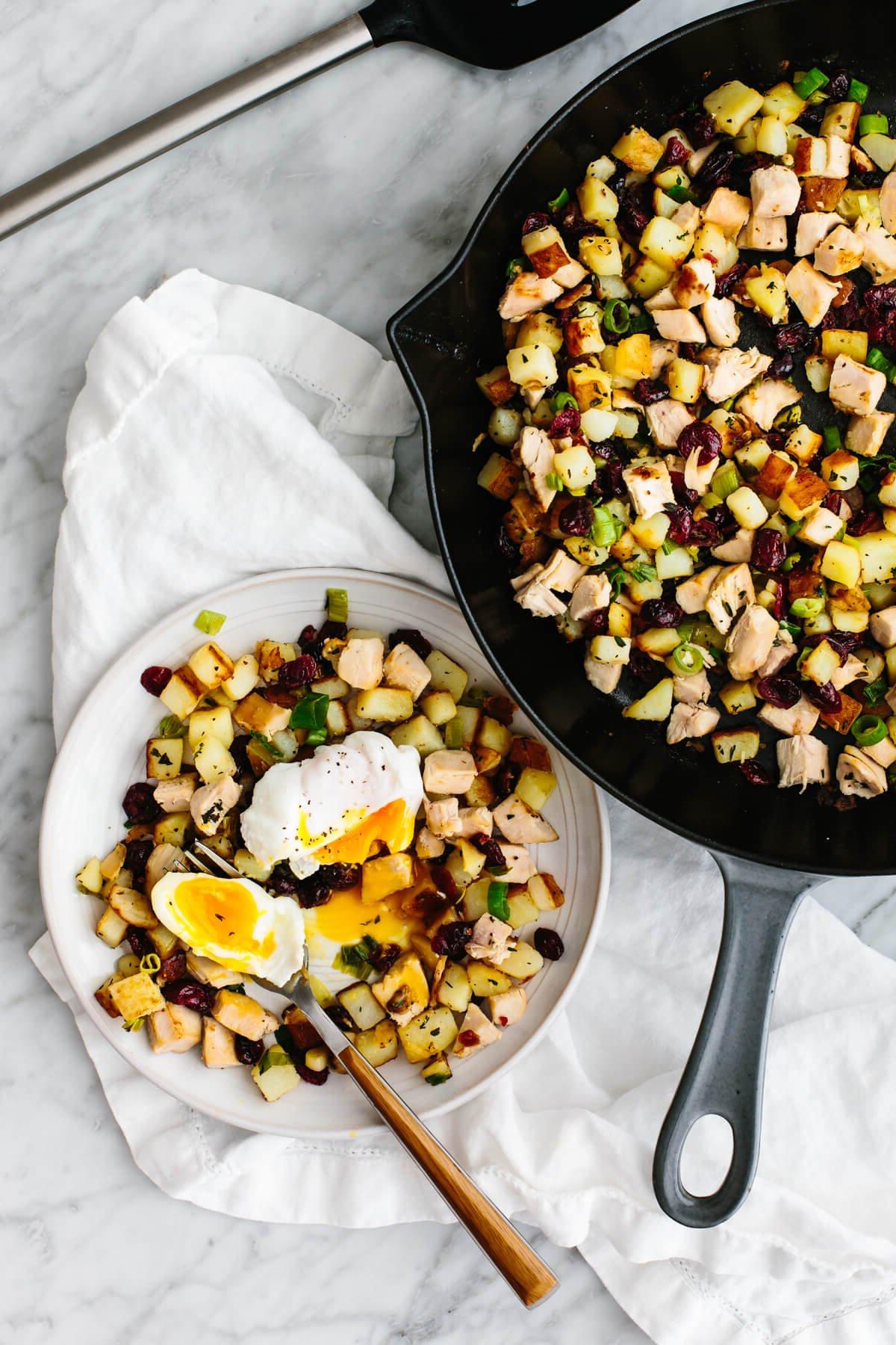 Begeisternde Truthahnreste-Rezepte 4 Ein Teller Truthahn-Cranberry-Hash mit pochiertem Ei neben einer Bratpfanne.