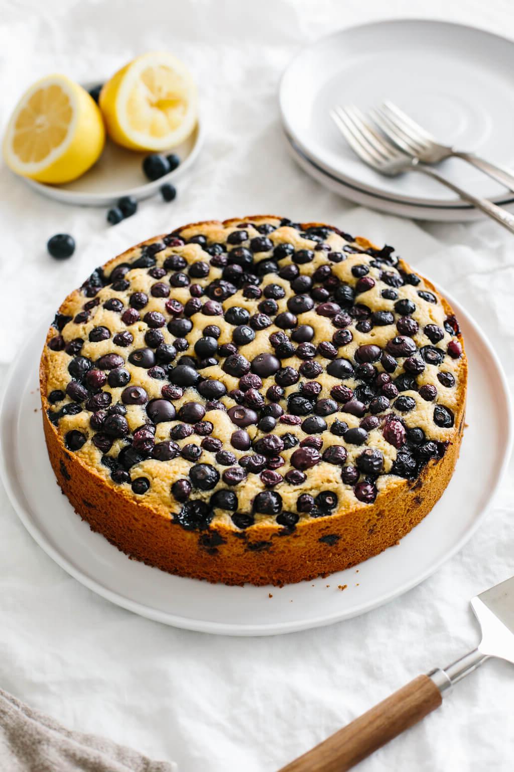 Über 40 Osterrezepte: Frisch, klassisch und einfach 51 Ein Zitronenkuchen, belegt mit Blaubeeren auf einem Tisch. Ein kleiner Teller mit frischen Zitronen und Blaubeeren steht daneben.