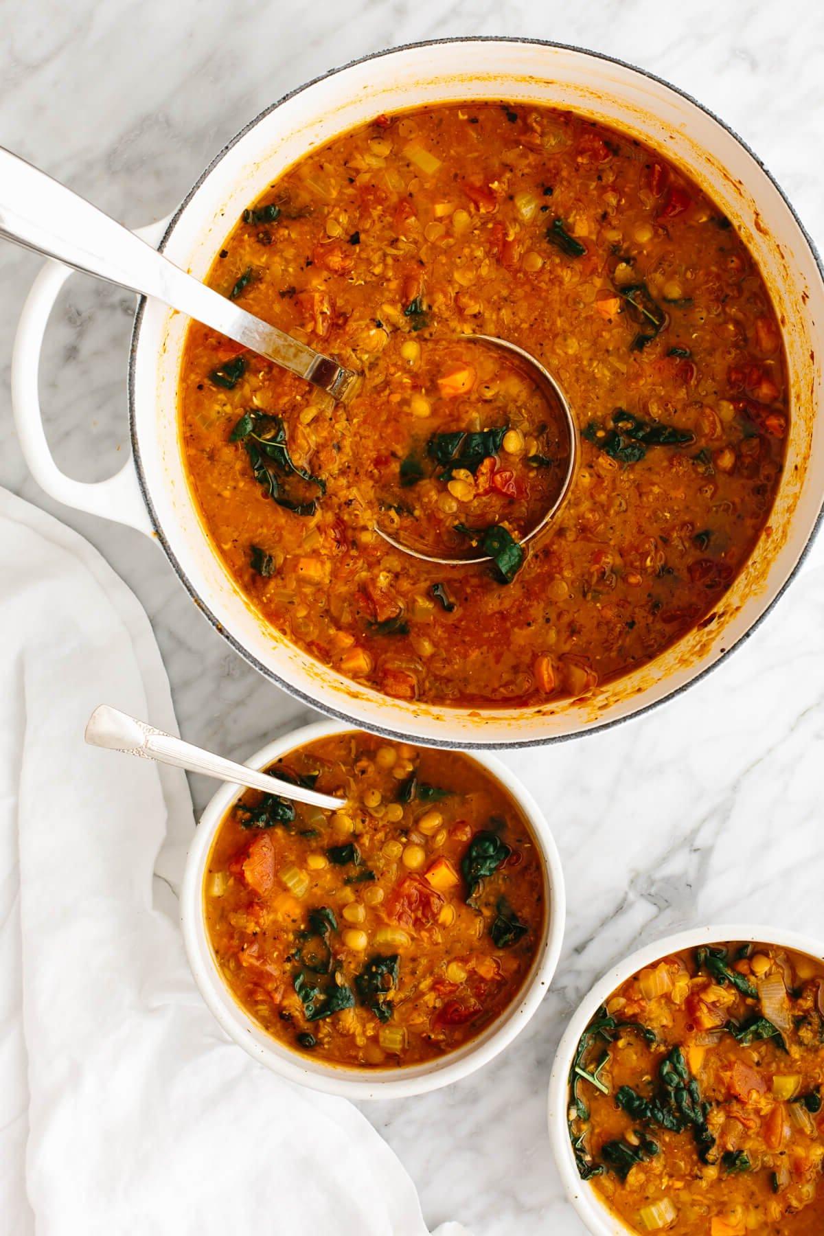30+ Gesunde Mittagessen-Ideen 7 Ein weißer Topf mit Linsensuppe neben Suppenschüsseln.