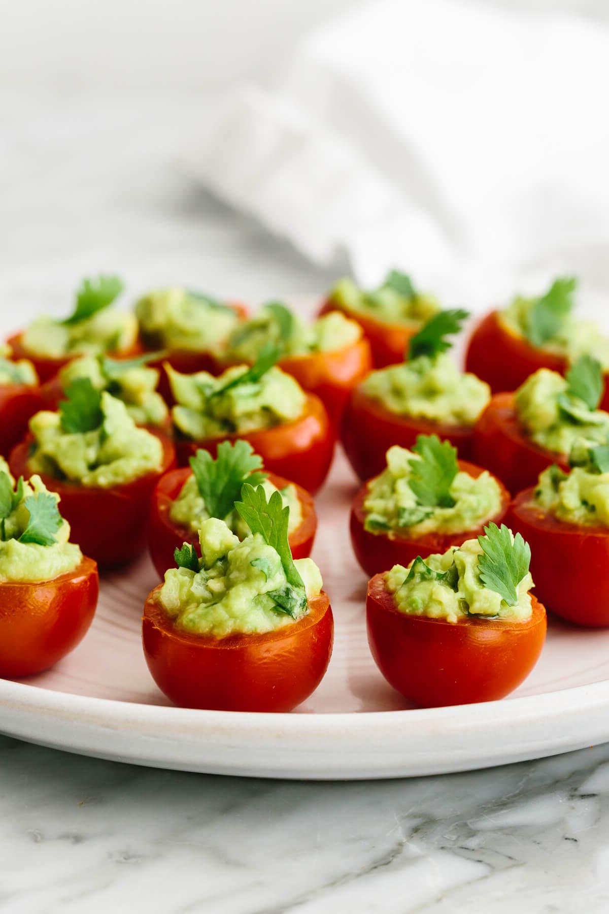 30+ Avocado Rezepte zum Genießen 7 Mit Guacamole gefüllte Tomaten auf einem Teller.