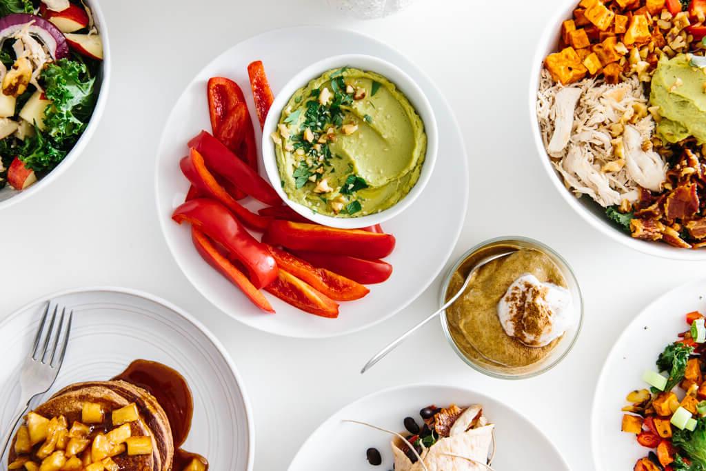Eine Auswahl an gesunden Meal-Prep-Gerichten für den Herbst auf einem weißen Tisch, bereit zum Essen, was die Bequemlichkeit und Ästhetik des vorbereiteten Kochens hervorhebt.
