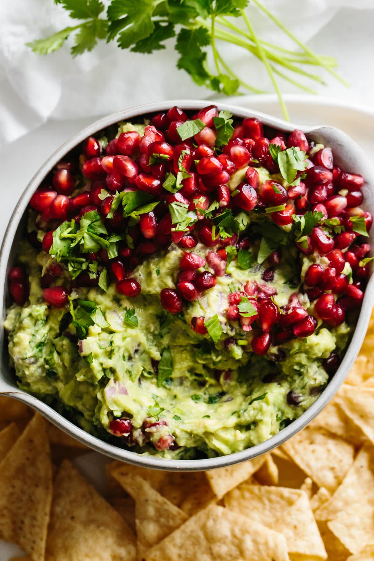 30+ Avocado Rezepte zum Genießen 8 Granatapfel-Guacamole in einer Schüssel, umgeben von Tortilla-Chips.