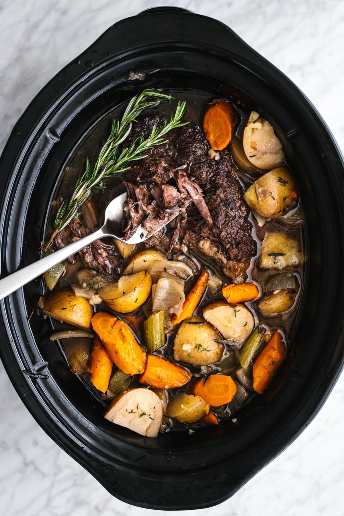 Das beste hausgemachte Rinderbraten-Abendessen, einfach im Schongarer zubereitet, mit zartschmelzendem Chuck Roast und Gemüse, das in einem aromatischen Sud durchzogen ist. Schongarer-Rinderbraten mit großem Servierlöffel.