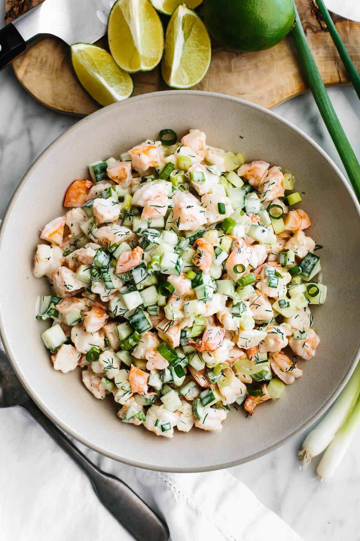 10+ beste Garnelenrezepte 8 Gurken-Garnelensalat in einer großen Servierschüssel neben Limetten.