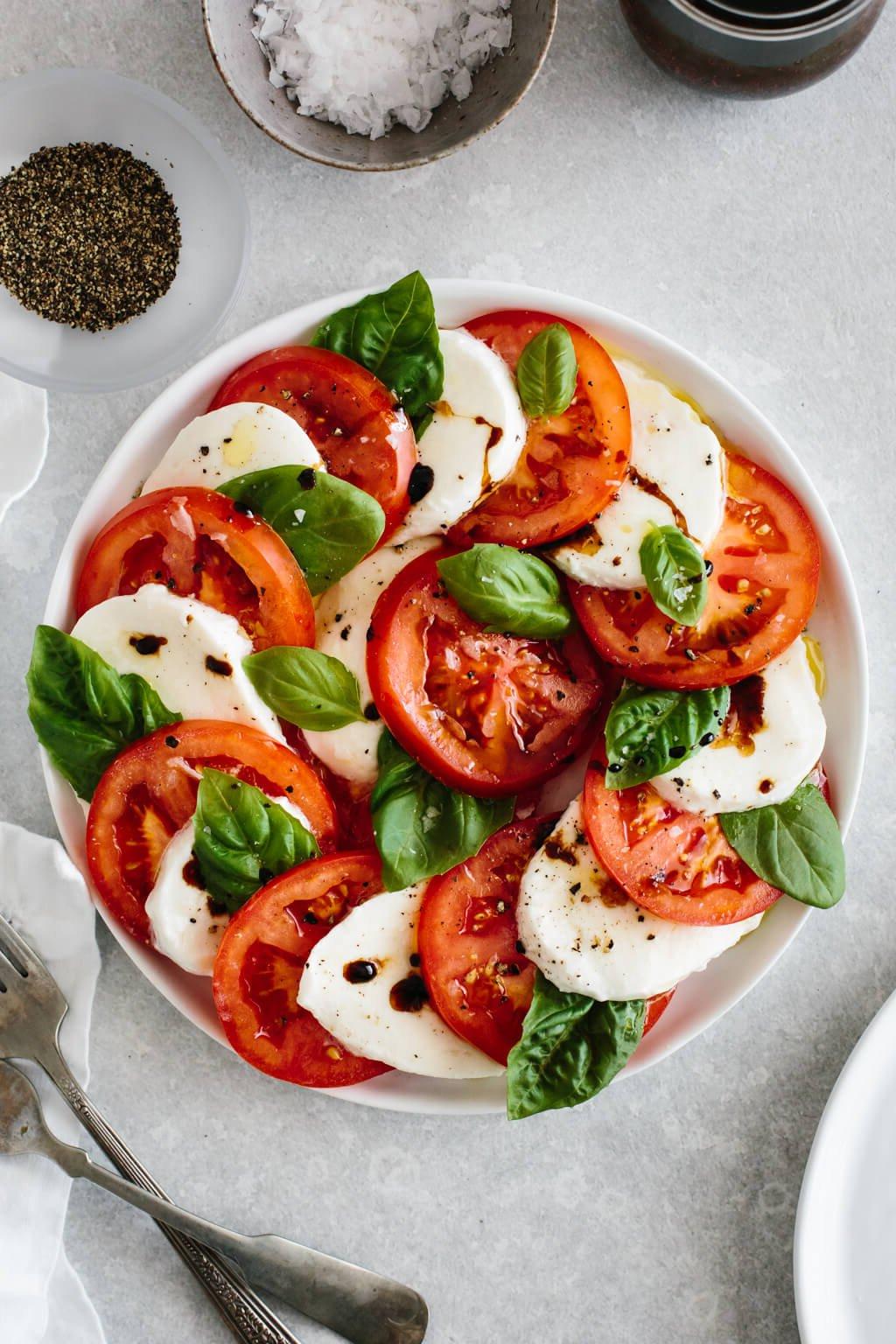 Die 60+ besten Mittelmeer-Diät-Rezepte 8 Tomaten- und Mozzarella-Scheiben auf einem Teller mit frischen Basilikumblättern.