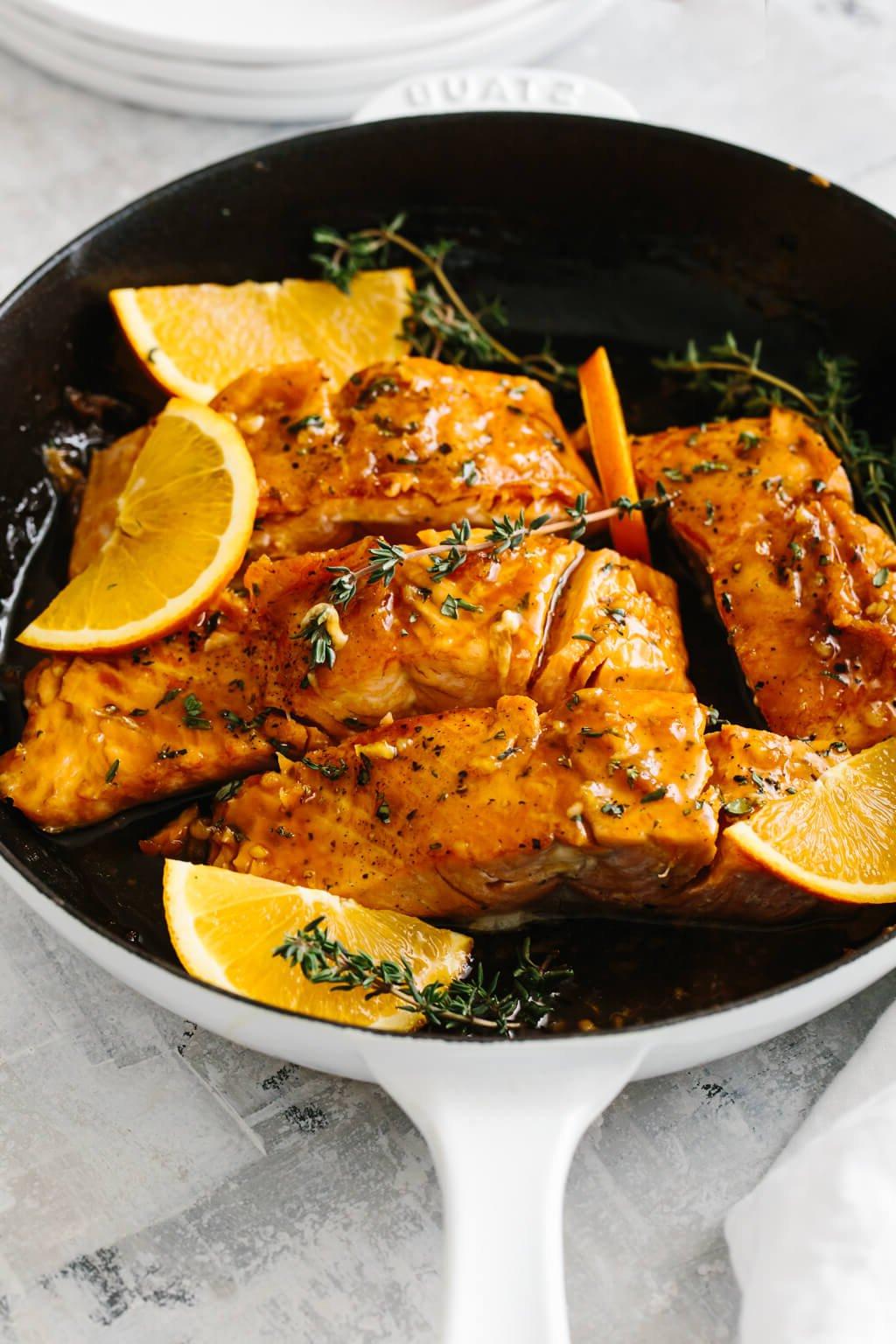Die 20+ besten Lachsrezepte 9 Vier Lachsfilets in einer Pfanne mit Orangenscheiben und Thymian darauf.