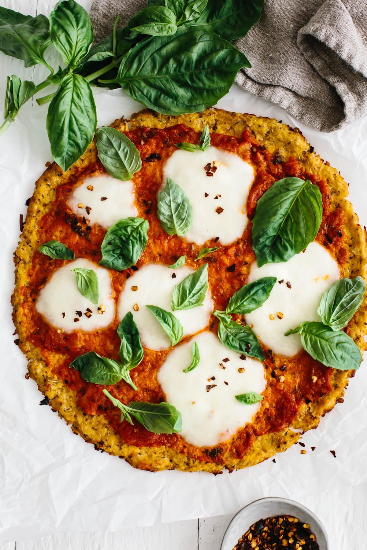 Blumenkohlpizzaboden belegt mit Marinara, Mozzarella und Basilikum.