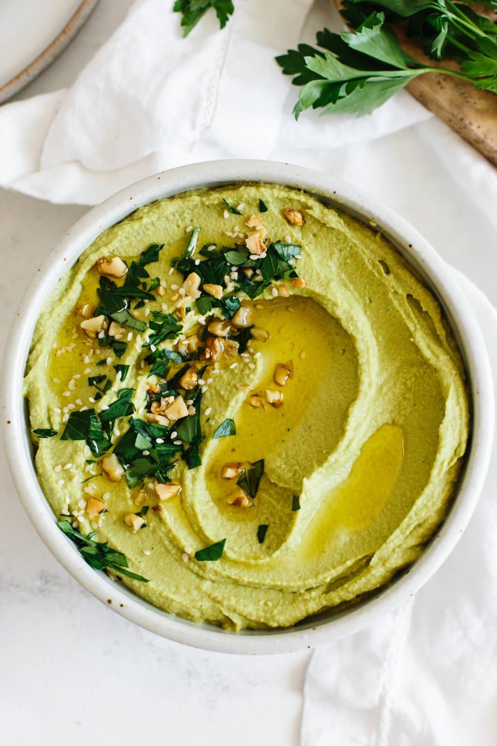 Eine Schale mit grünem Hummus, garniert mit Kräutern und Toppings.