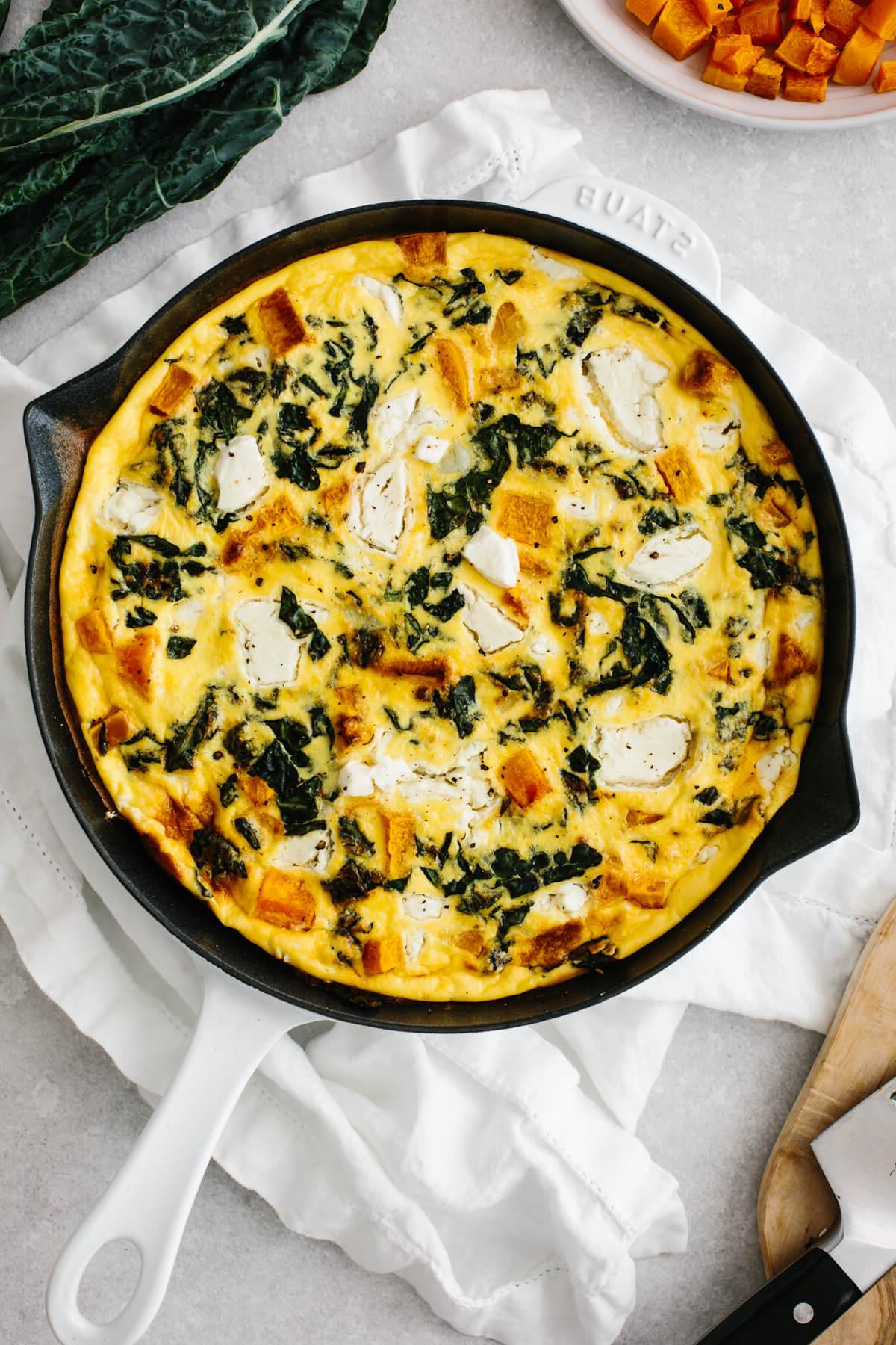 Die beliebtesten Weihnachtsfrühstücksideen 5 Butternusskürbis-Frittata in einer weißen Sauteuse auf einem Tisch.