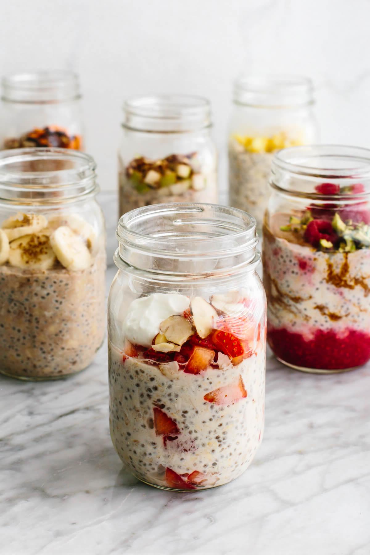Die beliebtesten Weihnachtsfrühstücksideen 6 Overnight Oats in mehreren Gläsern mit Früchten auf einem Tisch.