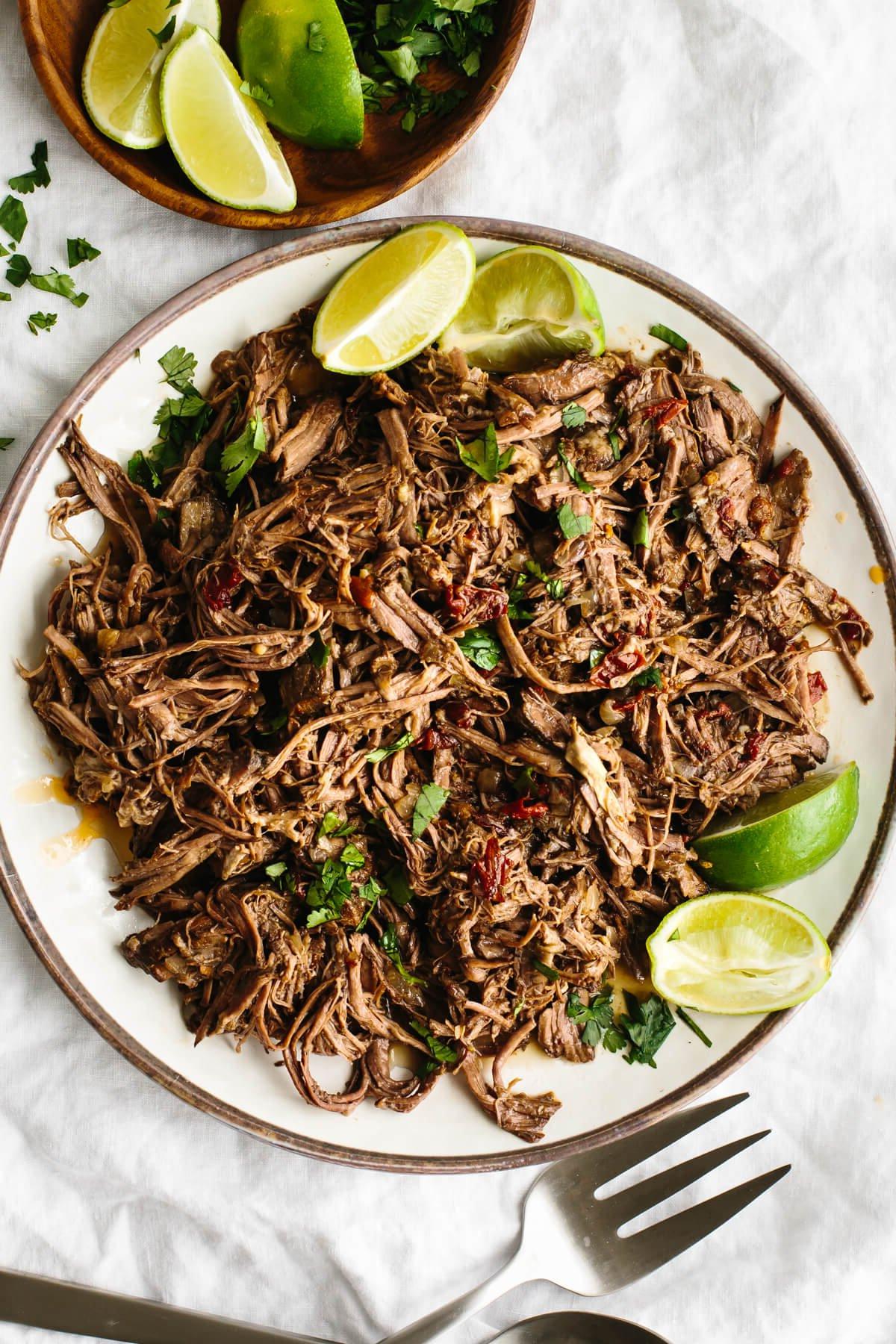 Rinder-Barbacoa auf einem Teller mit Limettenspalten.