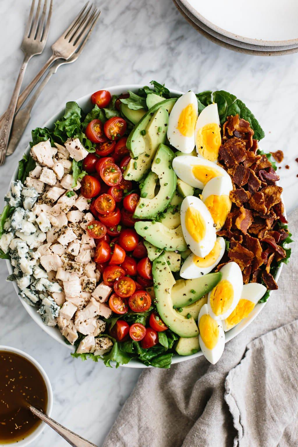 Cobb Salat mit Speck, hartgekochten Eiern, Avocado, Tomaten, gewürfeltem Hühnchen und Blauschimmelkäse in einer Schüssel auf einer Marmorarbeitsplatte.