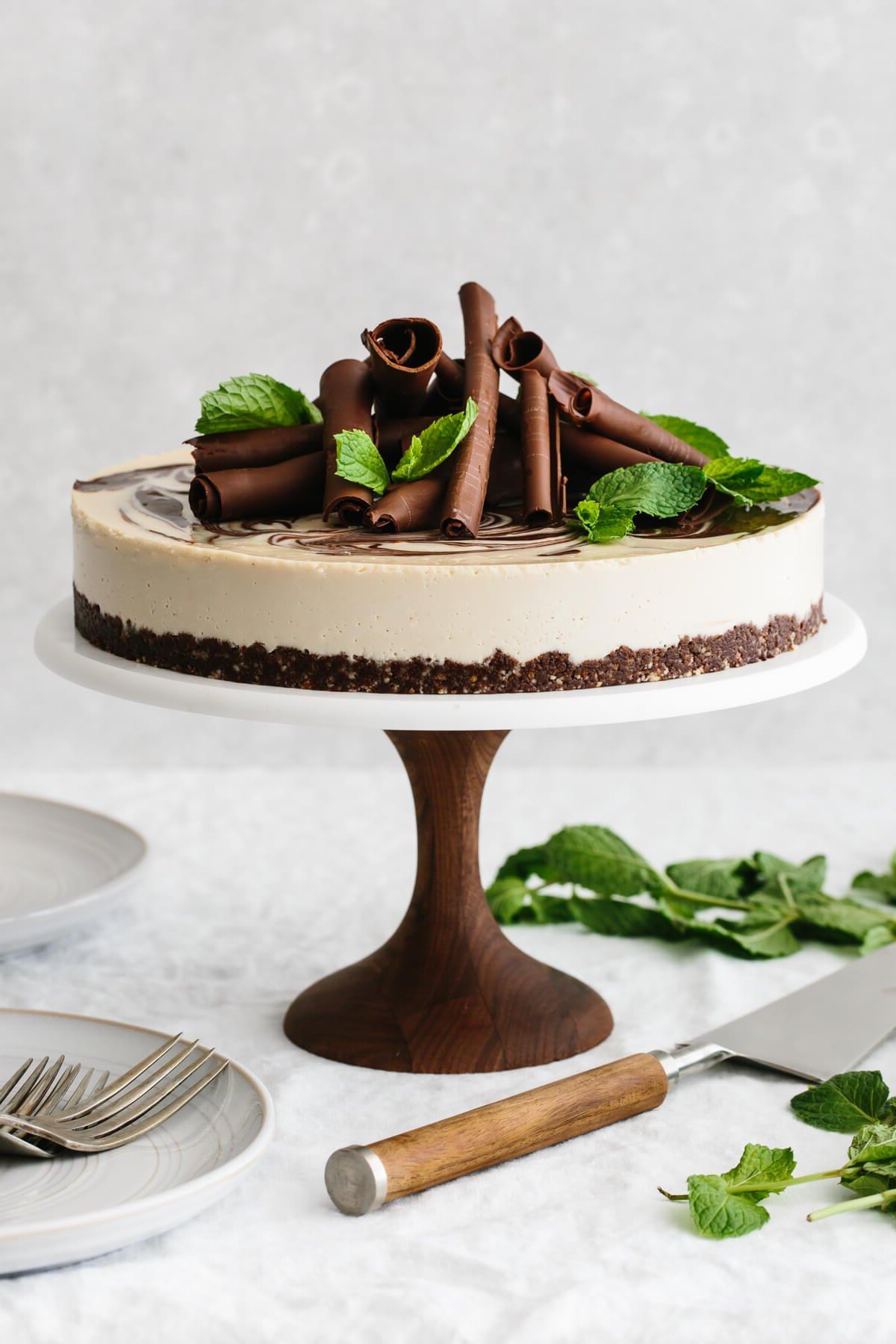 Minz-Schokoladen-Veganer Käsekuchen auf einem Tortenständer, garniert mit Schokoladenlocken und Minzblättern.